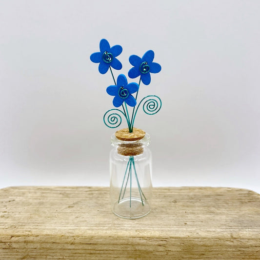 Little glass bottle with three blue wooden flowers sat on driftwood