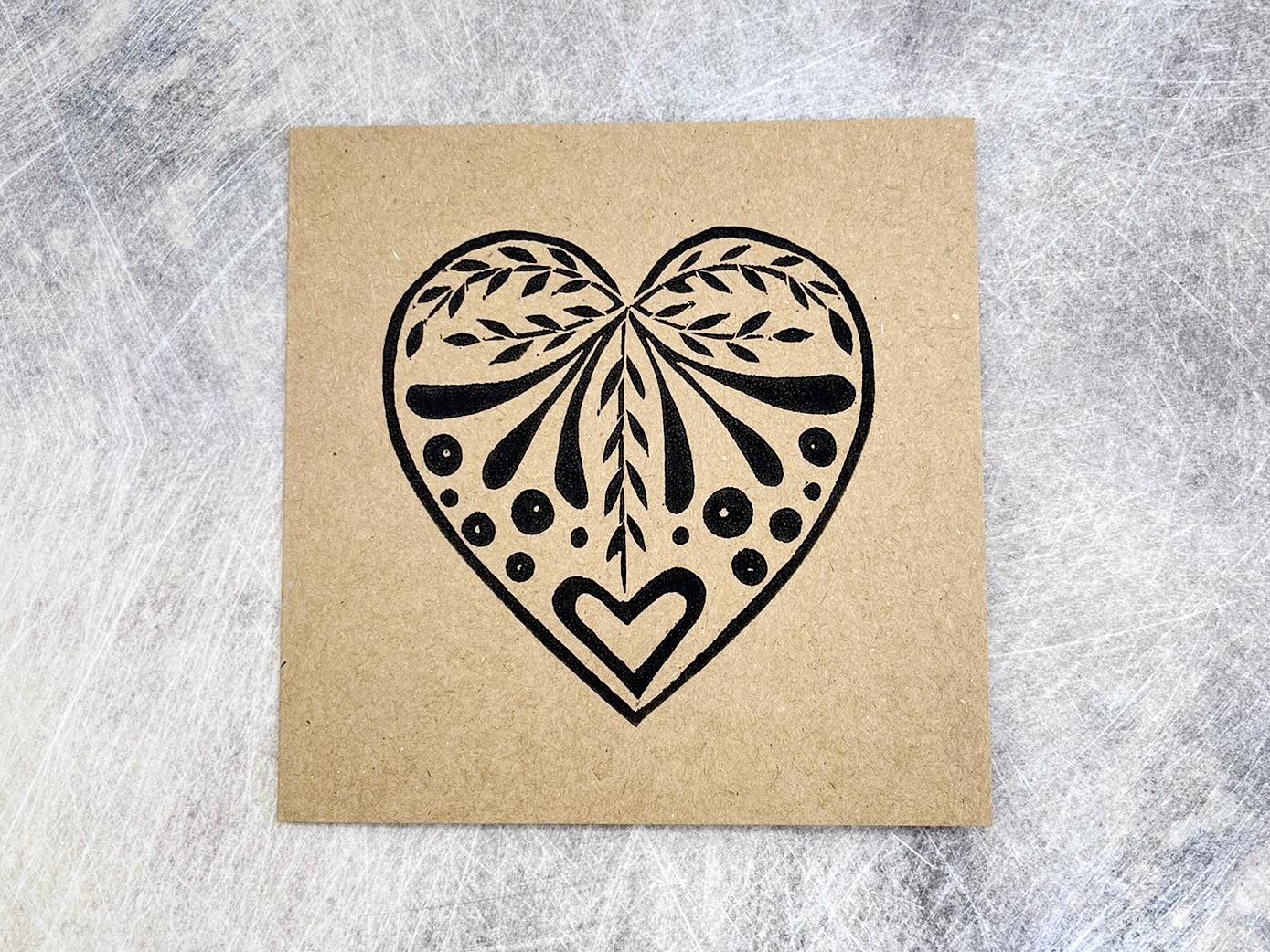 Card with an original lino printed black heart design on Kraft card laid on a textured surface. 