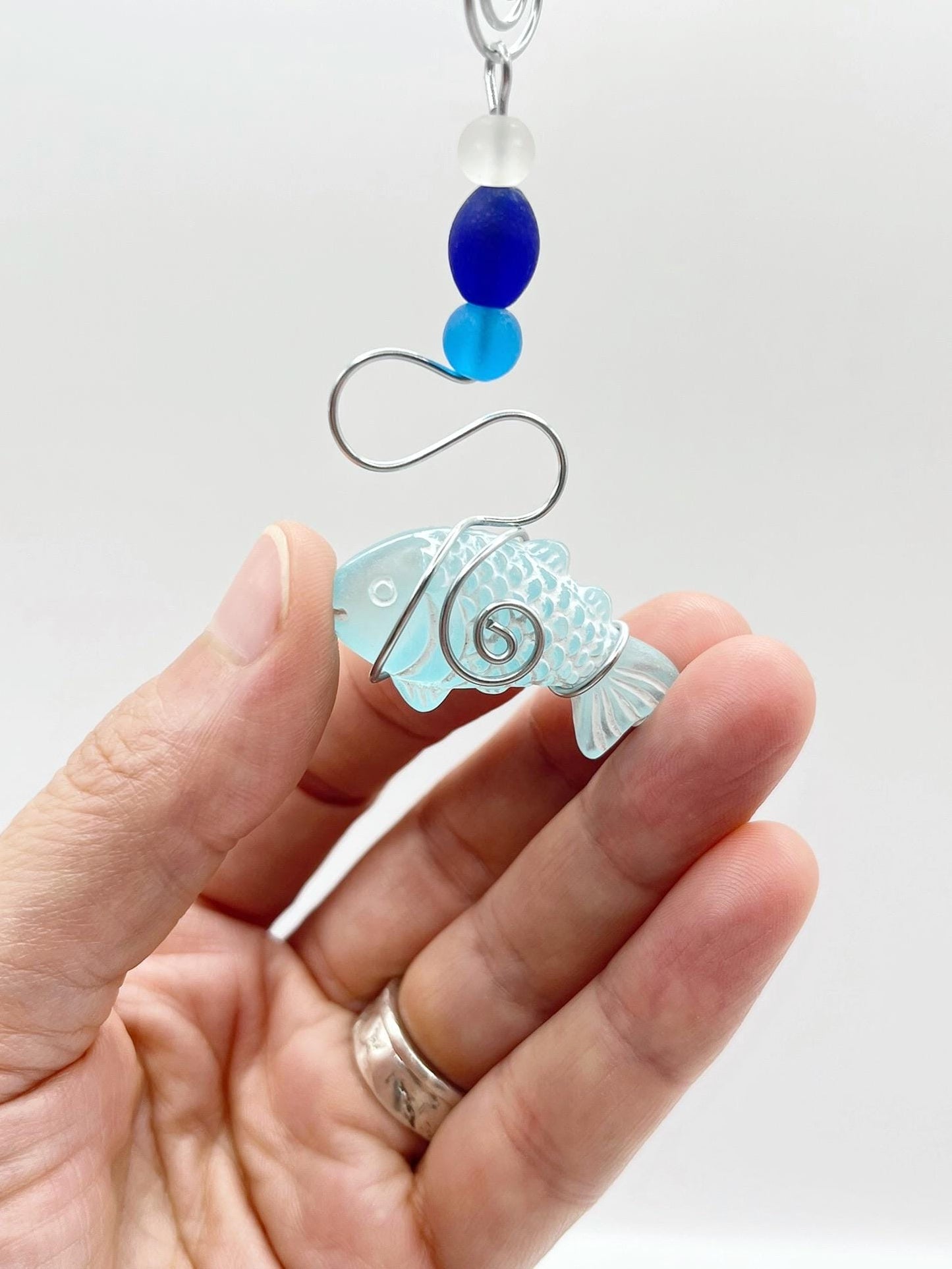 Decorative hanging fish ornament with wire and blue beads held in a hand against a white background