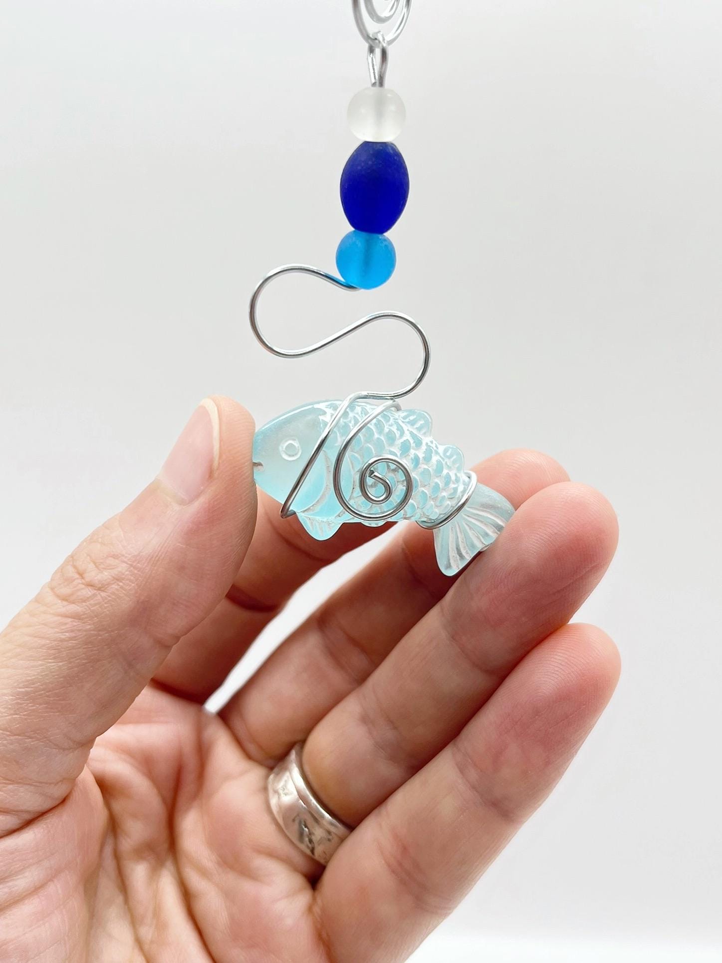 Decorative hanging fish ornament with wire and blue beads held in a hand against a white background