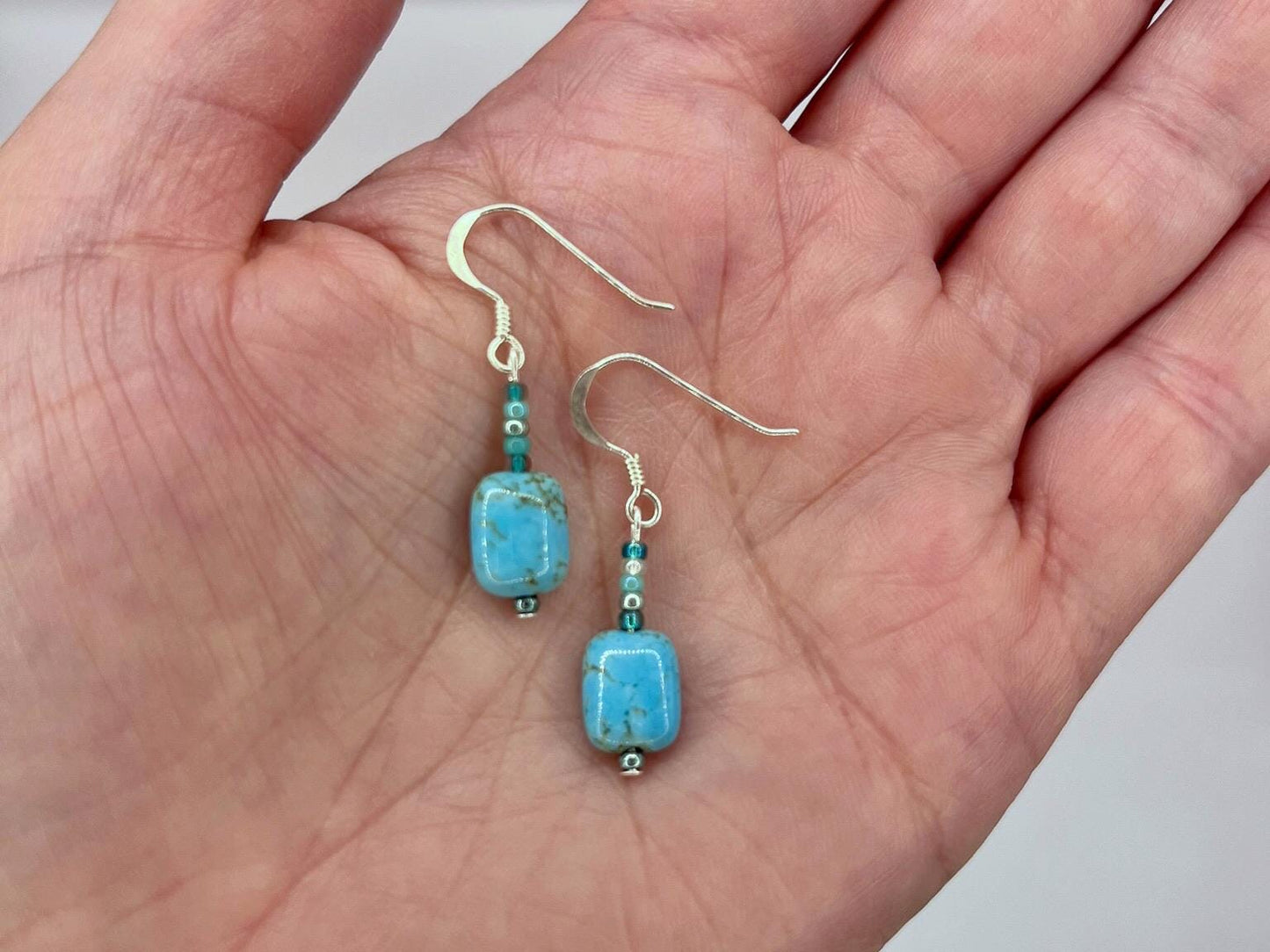 Turquoise beaded earrings held in a hand against a neutral background
