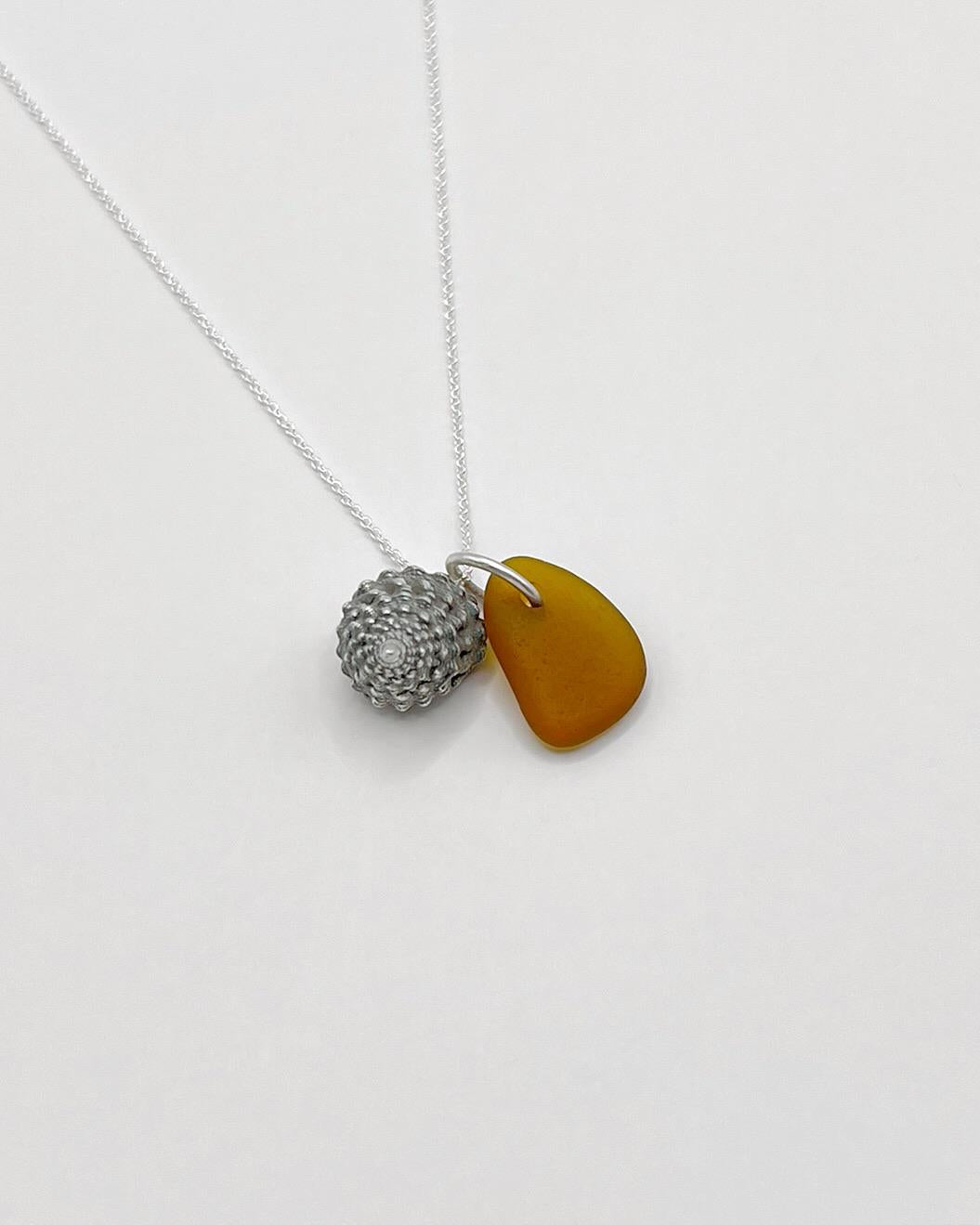 Necklace with burnt orange sea glass and silver shell pendant laid on a white background