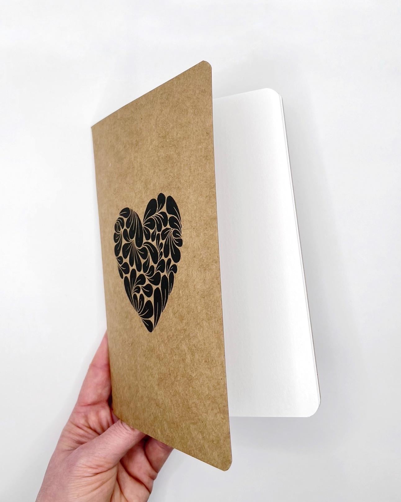 Kraft paper notebook with a floral heart design held by a hand on a white background
