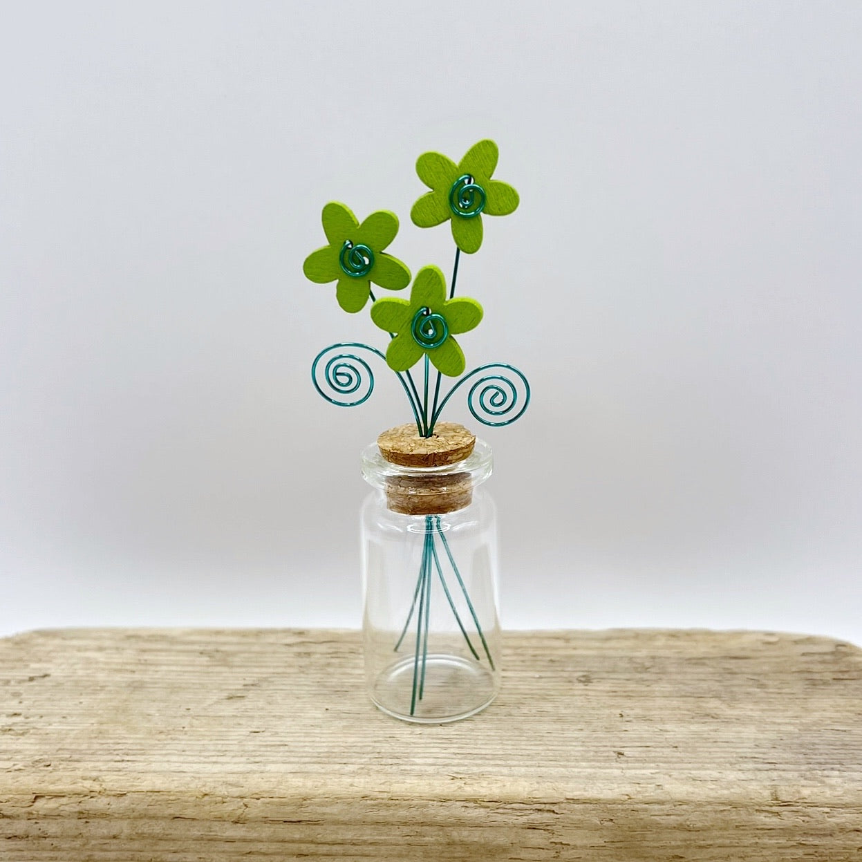 Little glass bottle with three green wooden flowers sat on driftwood