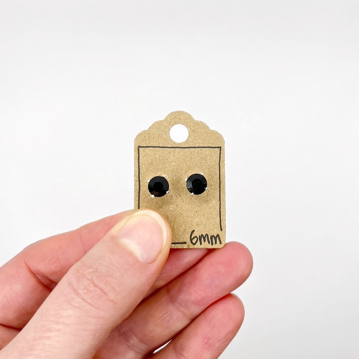 Black stud earrings on a cardboard tag held by a hand against a white background