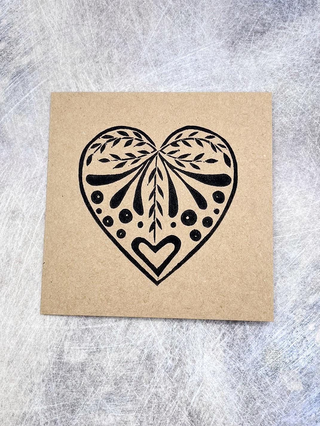 Card with an original lino printed black heart design on Kraft card laid on a textured surface. 