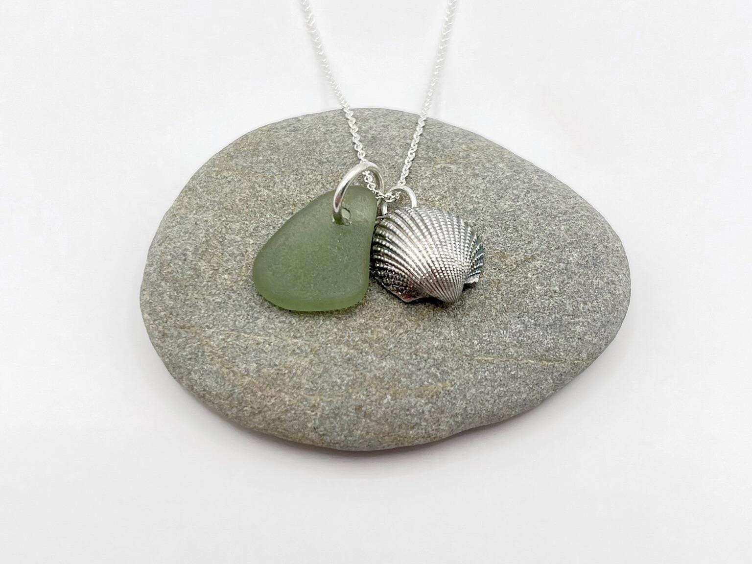 Necklace with green sea glass and silver shell pendant laid on a grey pebble