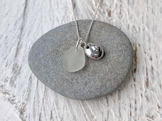 Necklace with a silver shell and sea glass pendant laid on a grey pebble against a textured surface