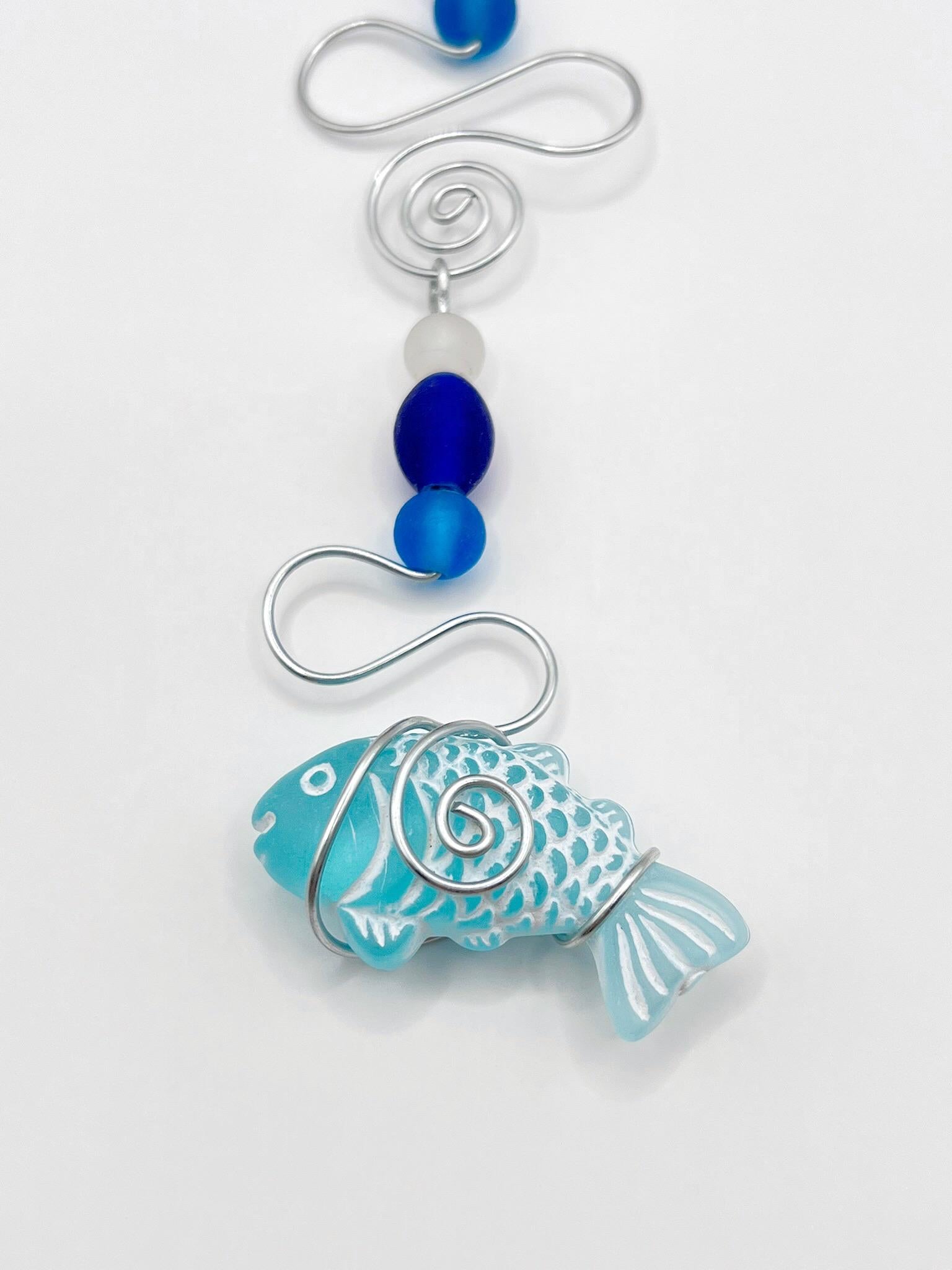Close up of decorative hanging fish ornament with wire and blue beads on a white background