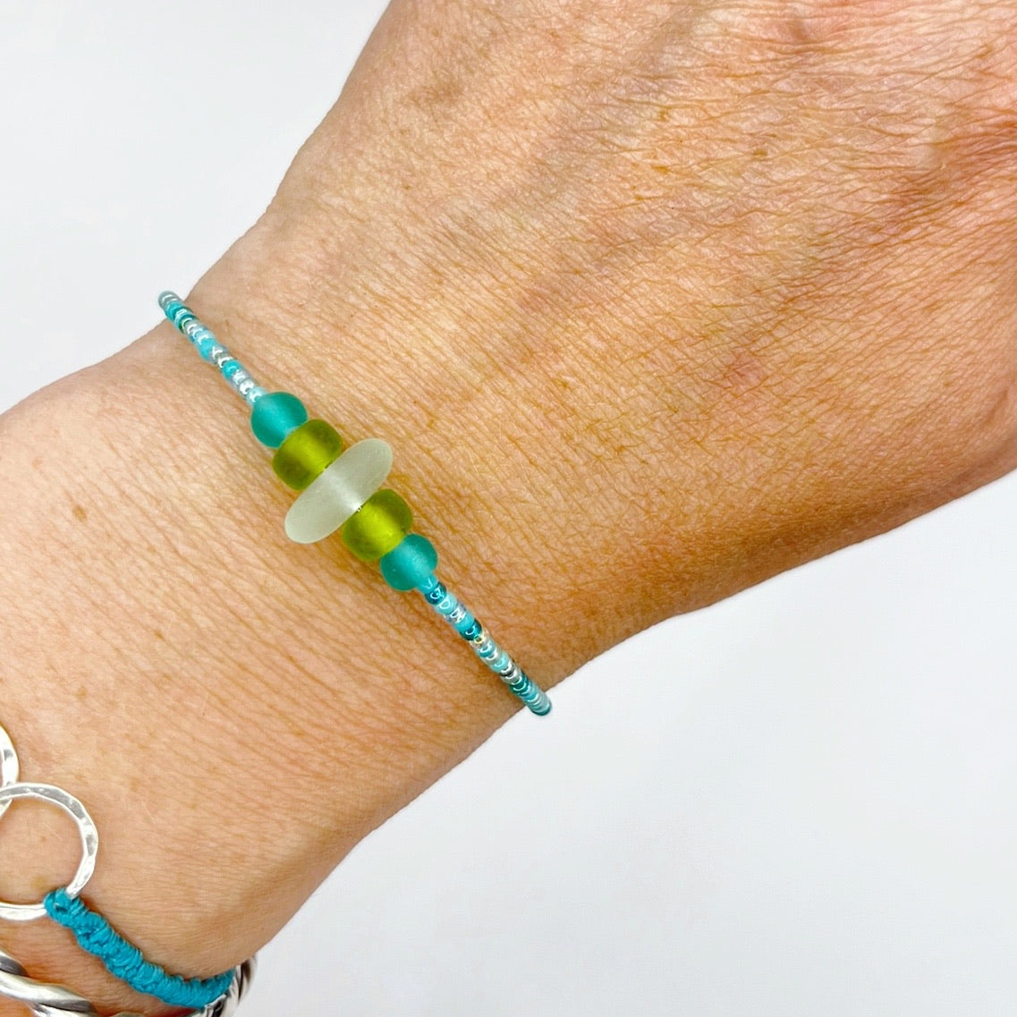A close-up of a person's wrist wearing the turquoise beaded bracelet with lime and sea green frosted glass beads and a piece of sea foam coloured Cornish sea glass.