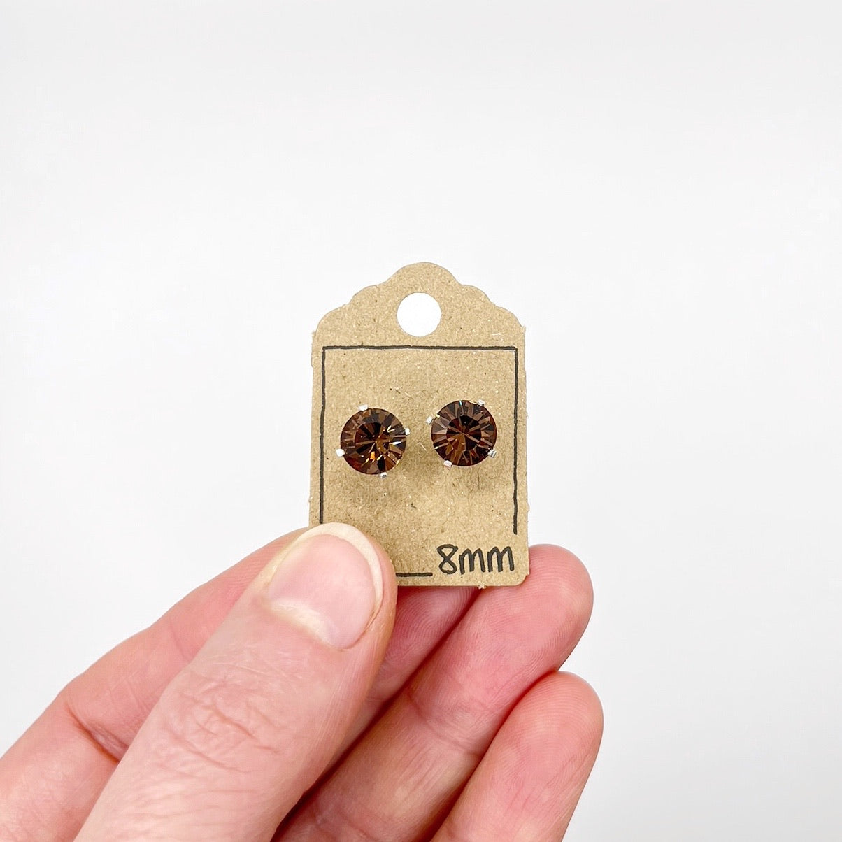 Cut glass stud earrings on a display card held by a hand against a white background