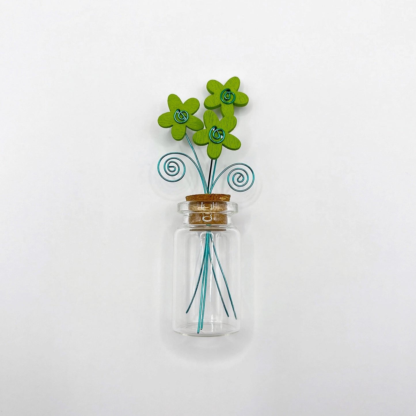 Little glass bottle with three green wooden flowers against a white background
