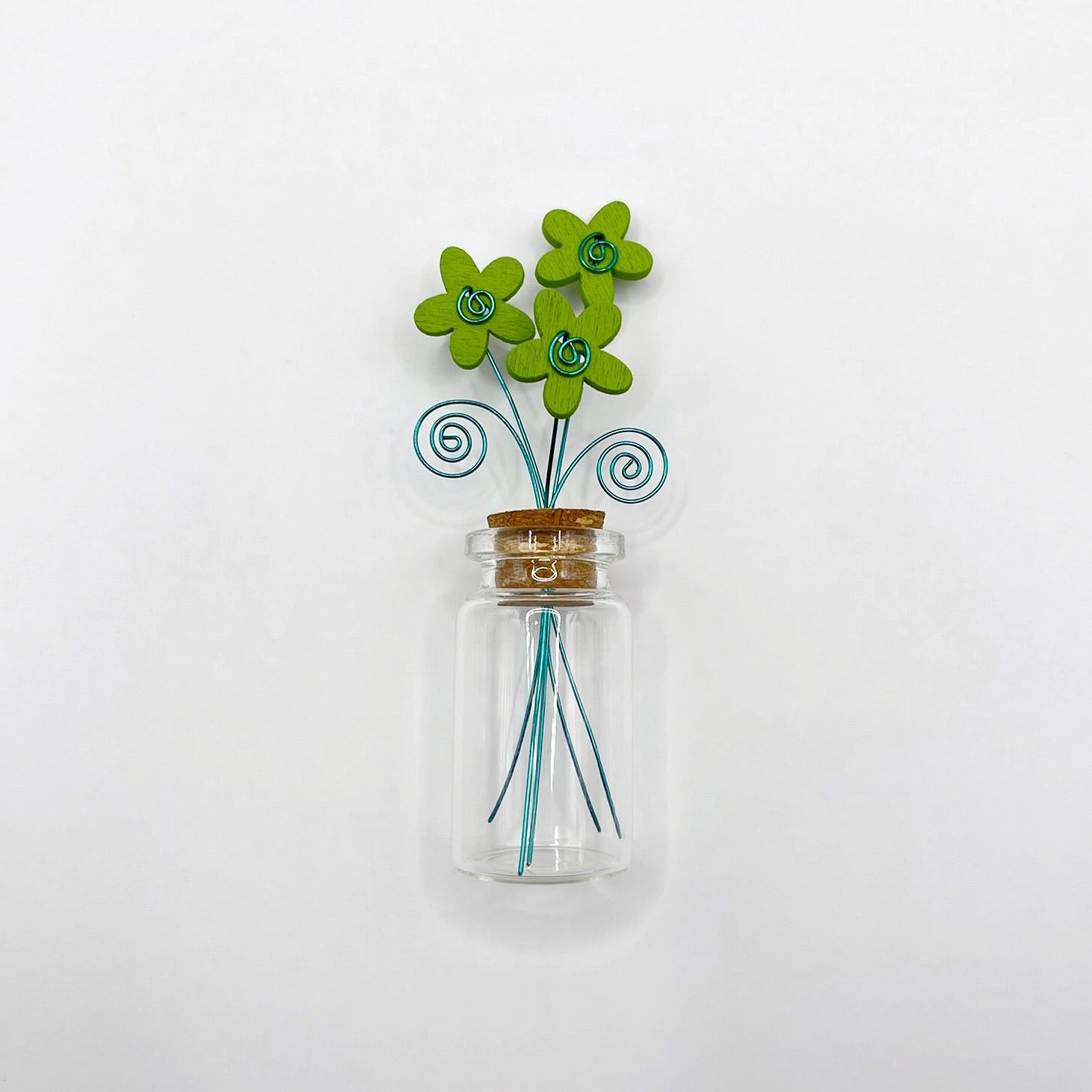 Little glass bottle with three green wooden flowers against a white background