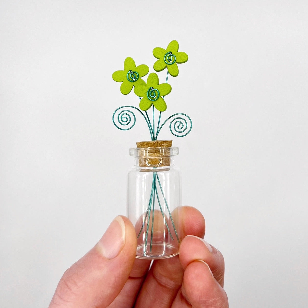 Little glass bottle with three green wooden flowers held in a hand against a white background