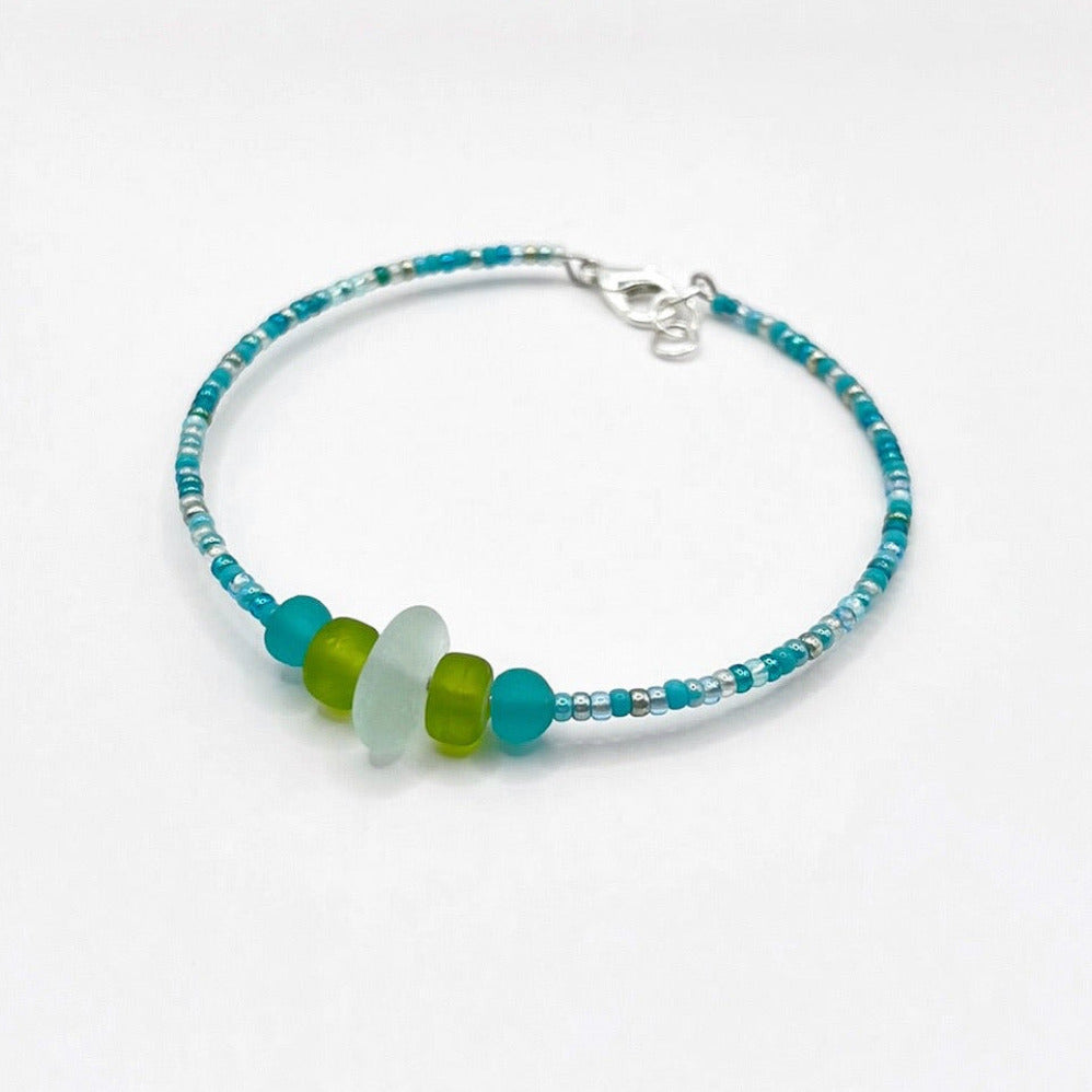 A turquoise beaded bracelet with lime and sea green frosted glass beads and a piece of sea foam coloured Cornish sea glass, finished with a silver plated lobster clasp and laid on a white background.