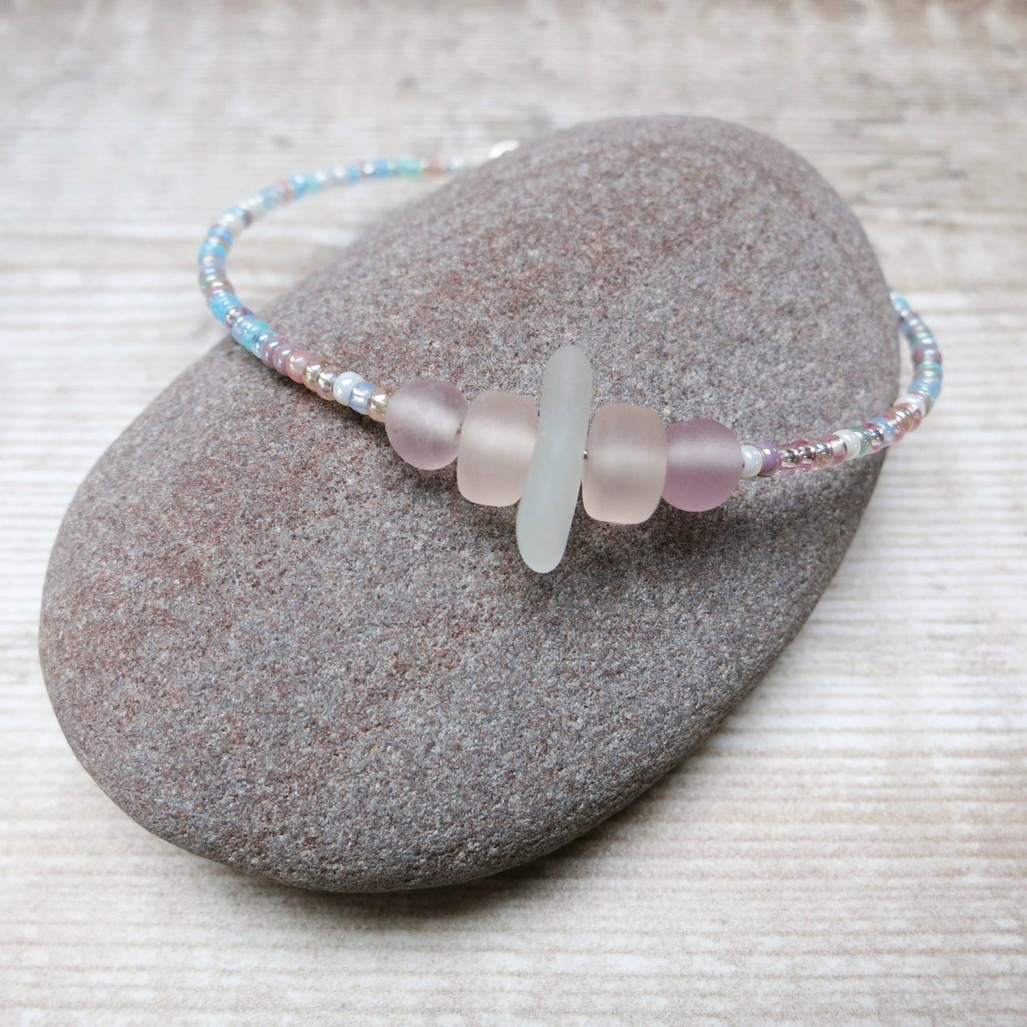 Bracelet with white sea glass and pastel beads laid on a purple pebble against a wooden background