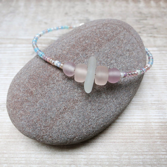 Bracelet with white sea glass and pastel beads laid on a purple pebble against a wooden background