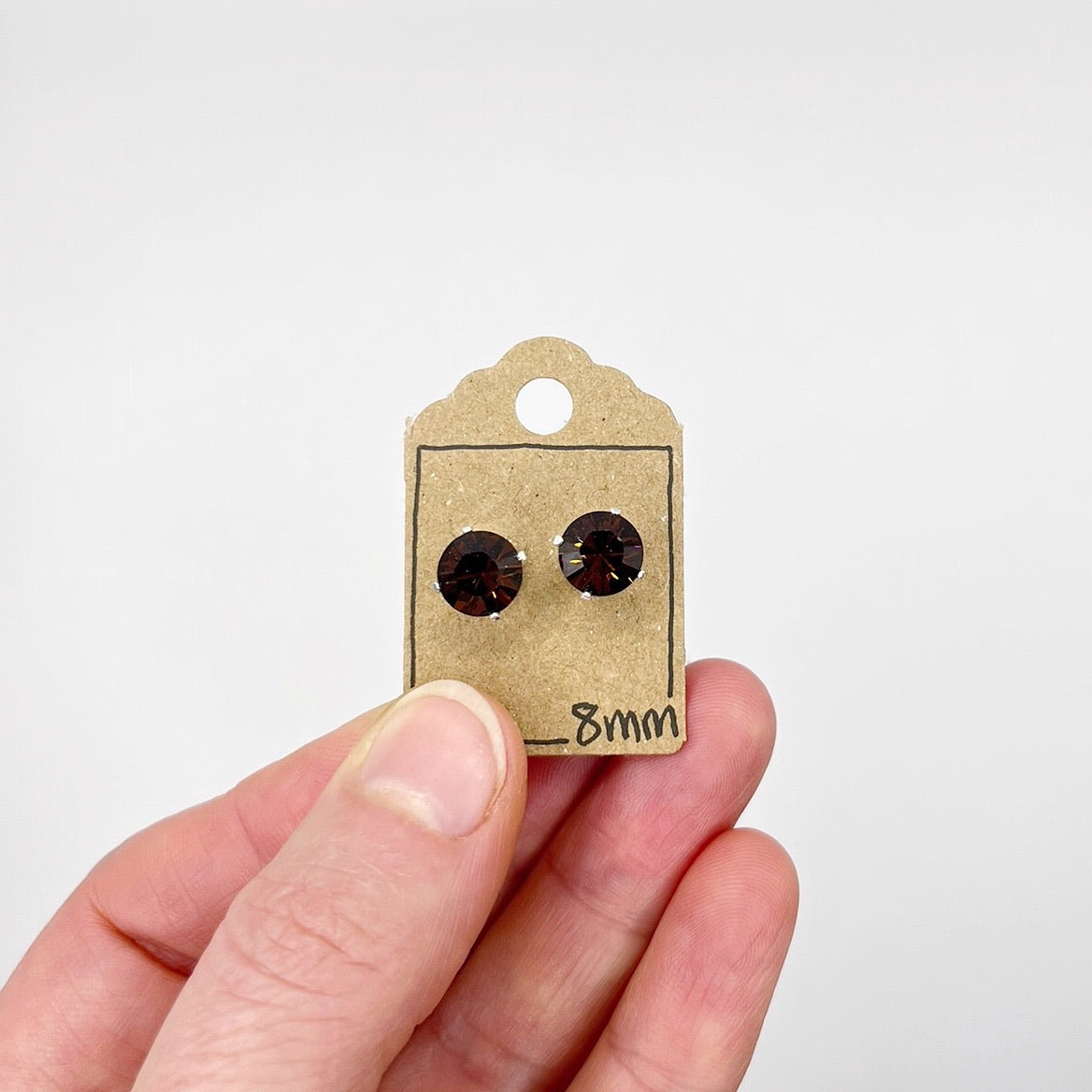 Cut glass stud earrings on a cardboard tag held by a hand against a white background
