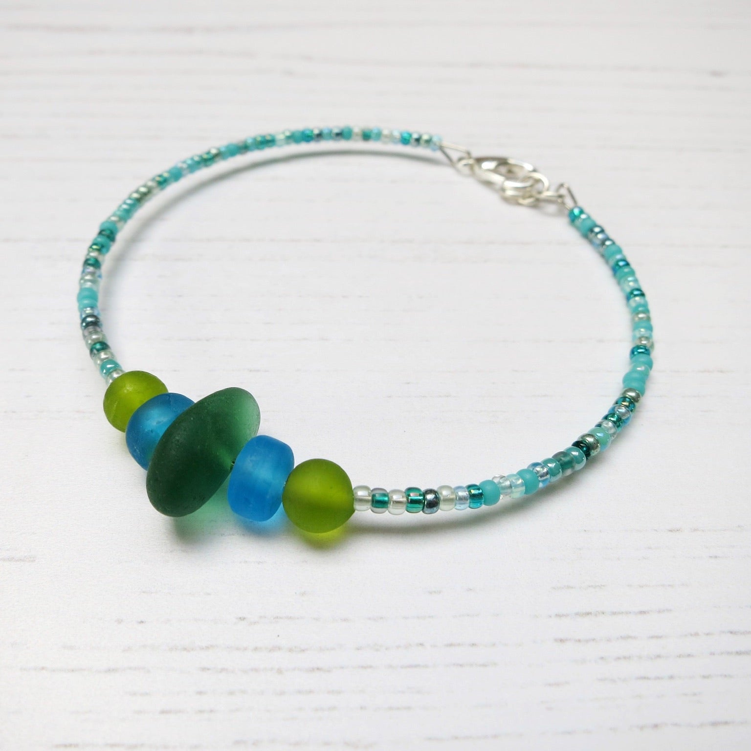 Bracelet with green sea glass and turquoise and green glass beads laid on a white background