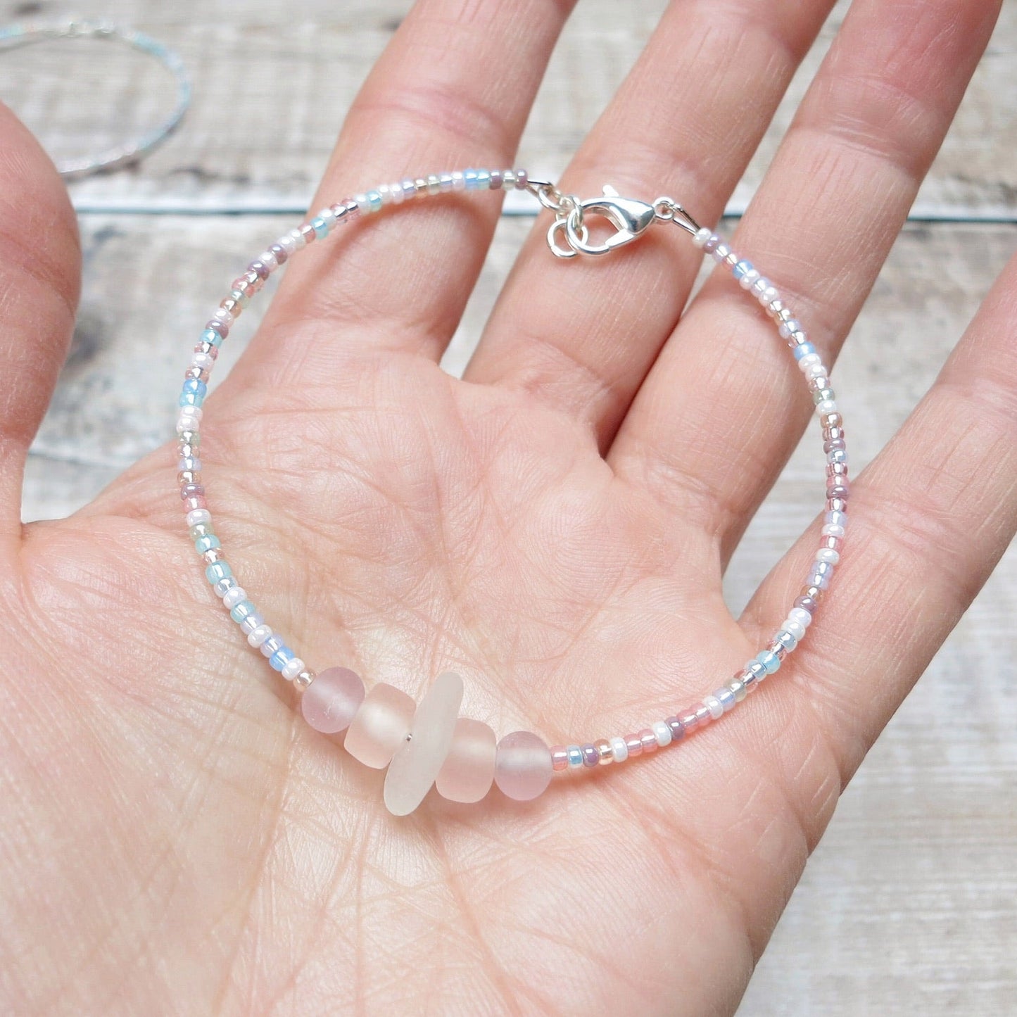 Bracelet with white sea glass and pastel beads held in a hand against a wooden background