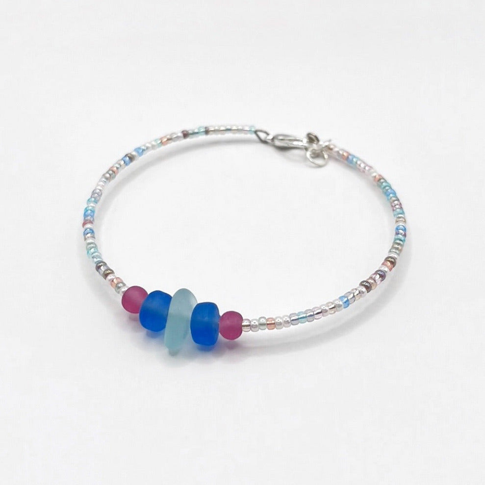 A pastel beaded bracelet with pink and blue frosted glass beads and a piece of sea foam coloured Cornish sea glass, finished with a silver plated lobster clasp and laid on a white background.