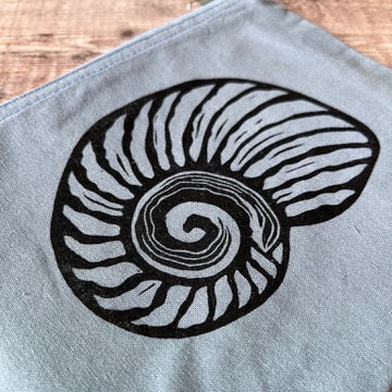 Close up of a light blue fabric pouch with a black printed nautilus shell design, resting on a rustic wooden plank background.