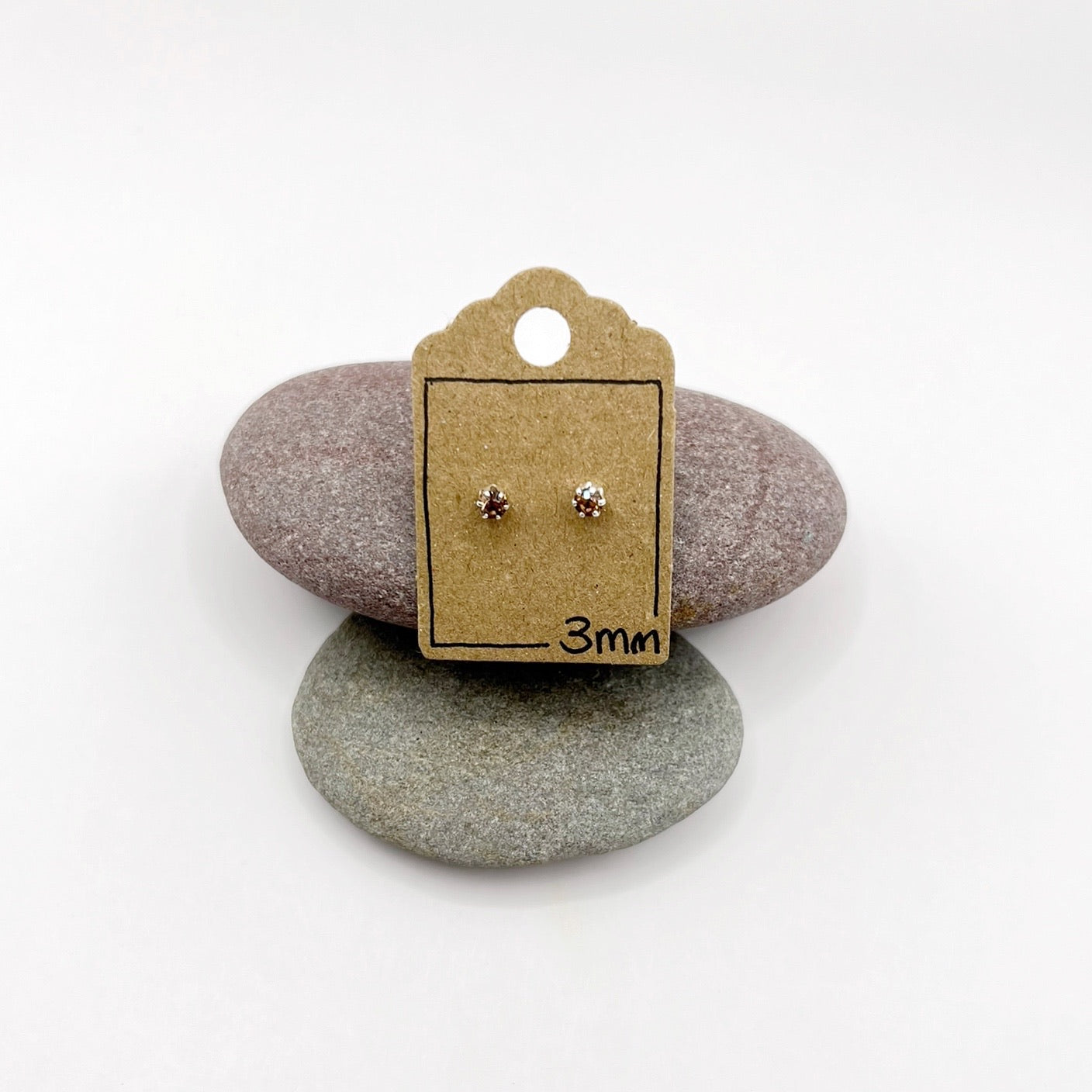 Pair of earrings on a cardboard backing with '3mm' text, placed on two stones.