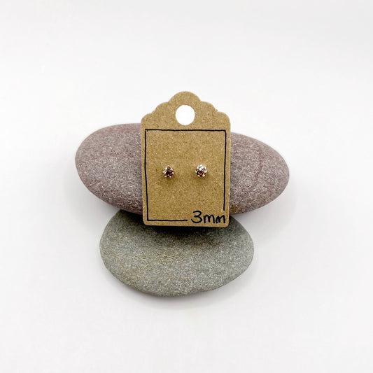 Pair of earrings on a cardboard backing with '3mm' text, placed on two stones.