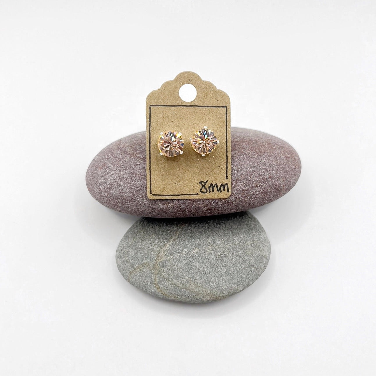 Pair of cut glass stud earrings on a cardboard backing card, placed on two stones with a white background.