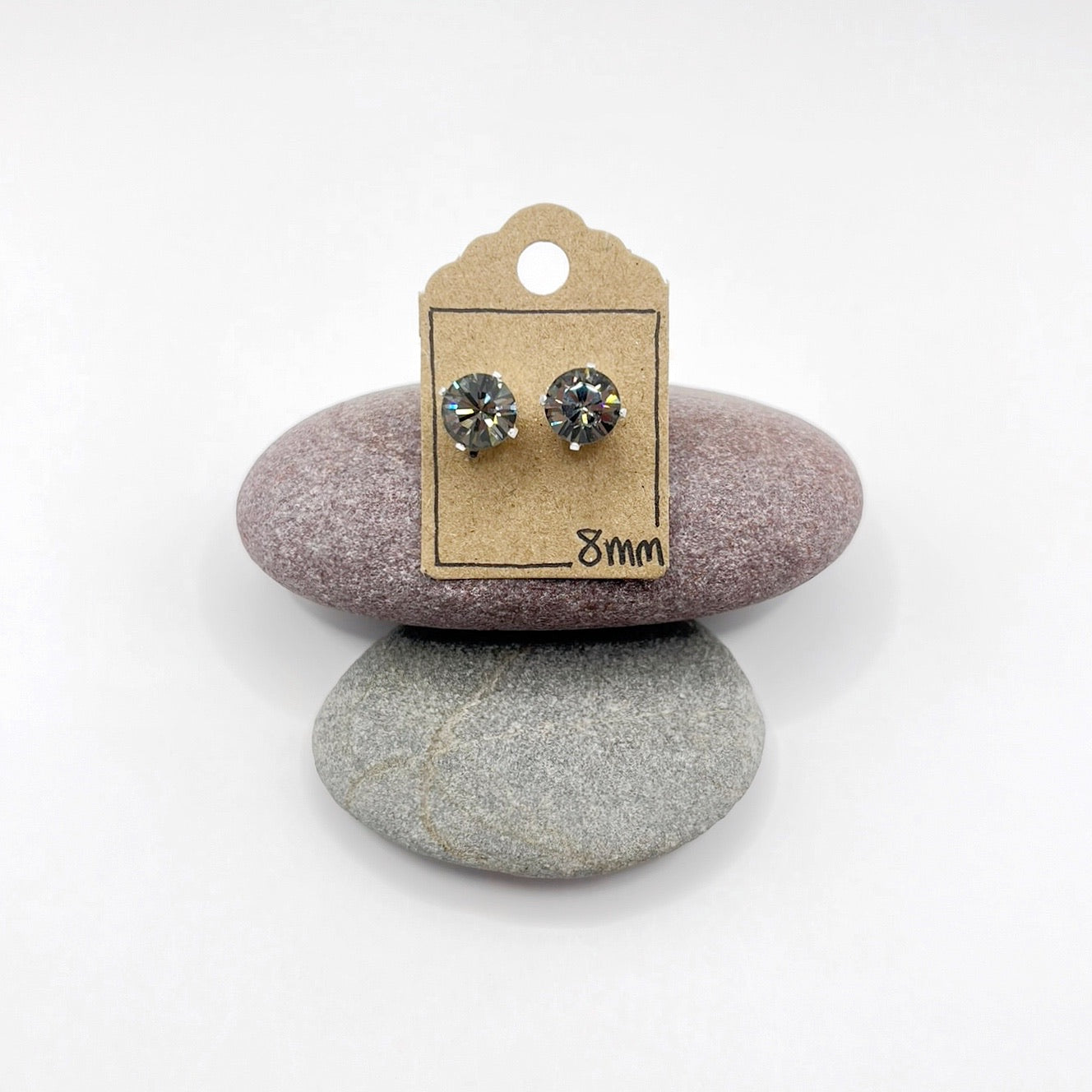 Pair of cut glass stud earrings on a cardboard backing card, placed on two stones with a white background.