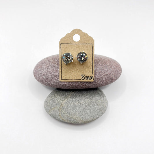 Pair of cut glass stud earrings on a cardboard backing card, placed on two stones with a white background.