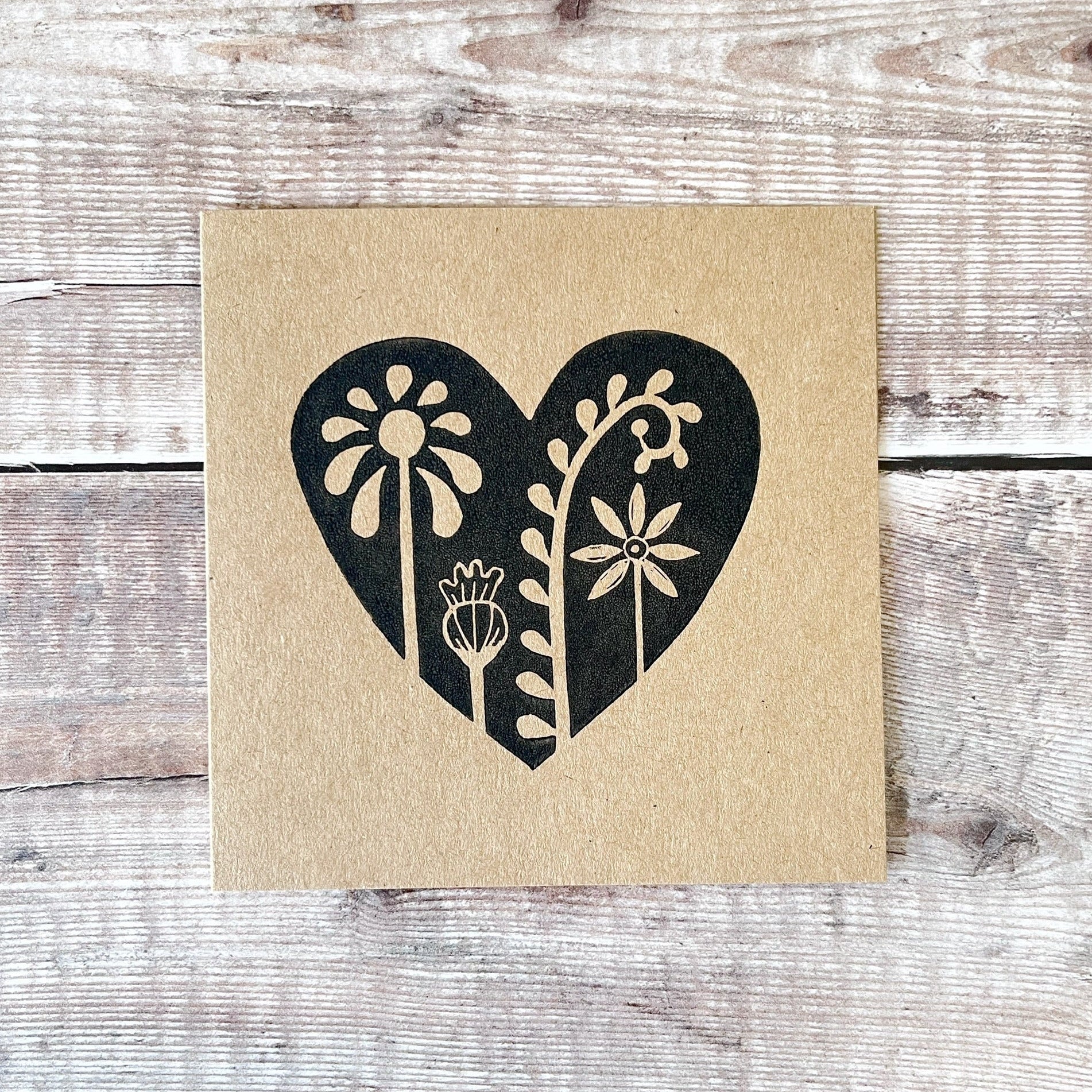 Floral heart design lino printed in black on kraft card and laid on a wooden background.