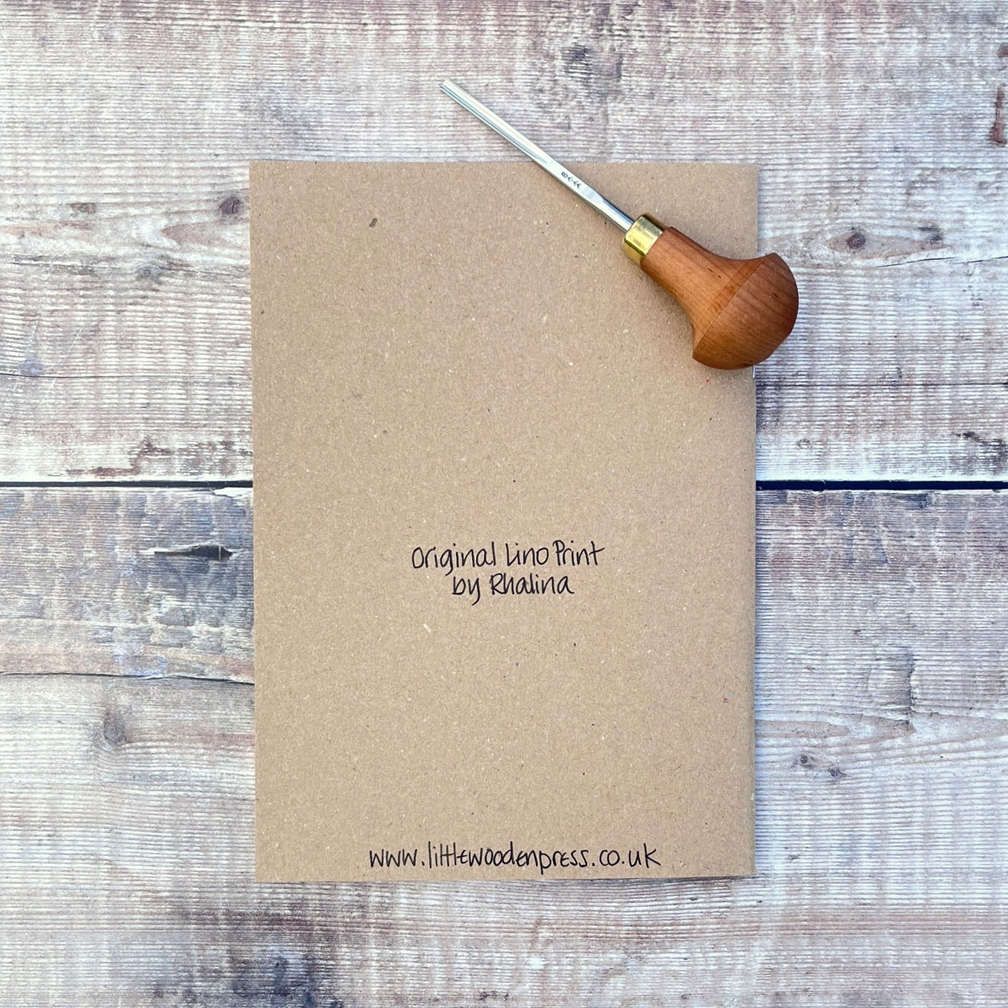 Kraft notebook with 'Original lino print by Rhalina' text and a lino cutting tool on a wooden surface.