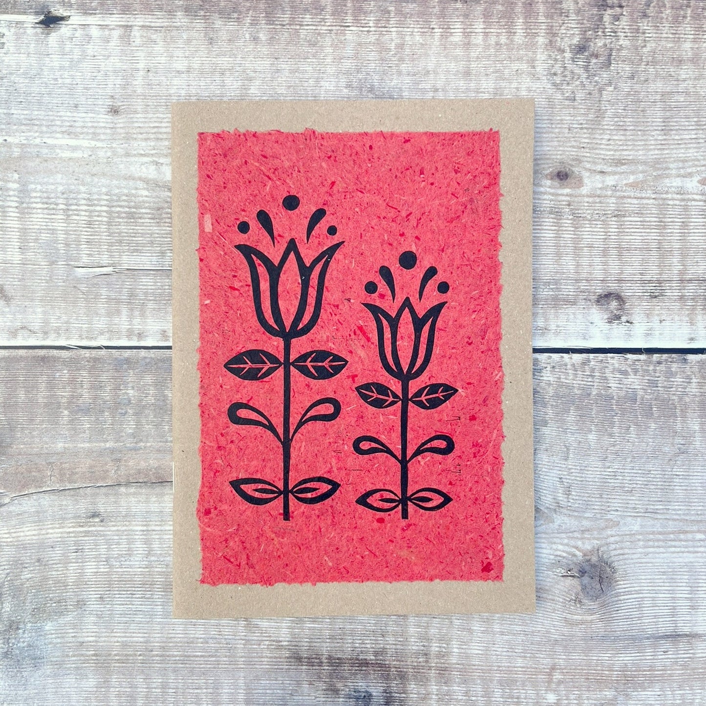 A5 kraft sketchbook with an original lino print of Tulips on handmade brick red paper. Laid on a wooden background.