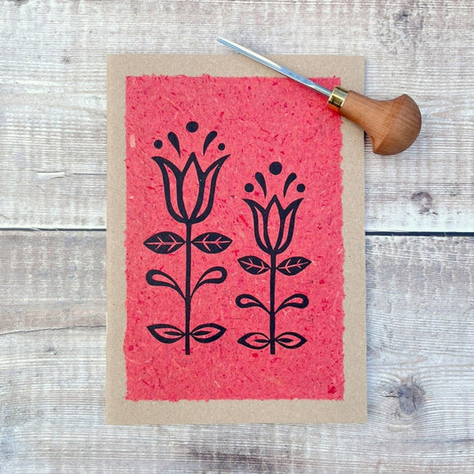 A5 kraft sketchbook with an original lino print of Tulips on handmade brick red paper. Photo includes lino cutting tool laid on a wooden background.