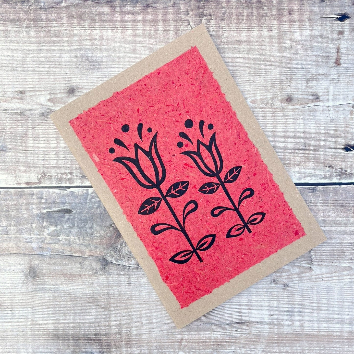 A5 kraft sketchbook with an original lino print of Tulips on handmade brick red paper. Laid on a wooden background.