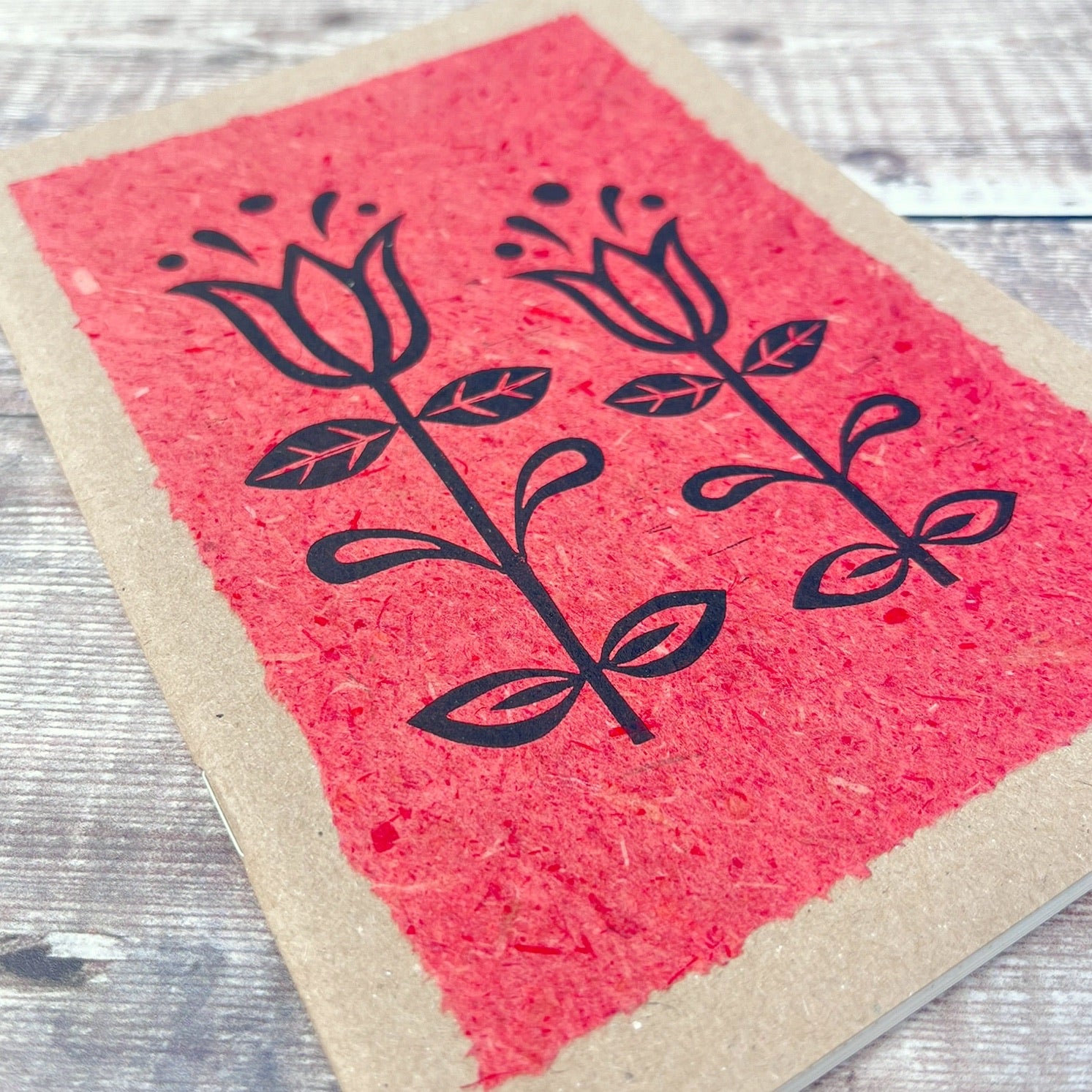 Close up of A5 kraft sketchbook with an original lino print of Tulips on handmade brick red paper. Laid on a wooden background.