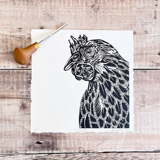 Black and white linocut of a chicken laid on a wooden surface with a carving tool.