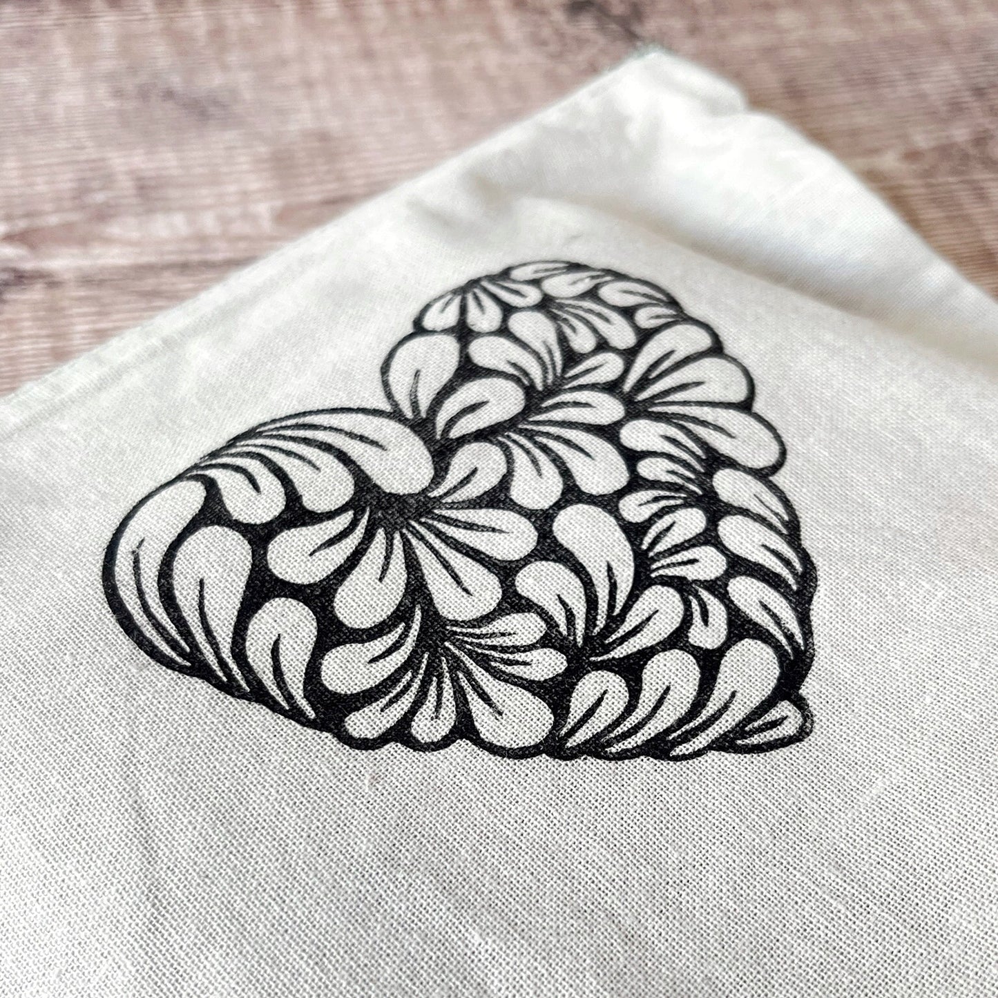 Close up of pale grey toiletry bag with lino printed heart design. Laid on a wooden surface.