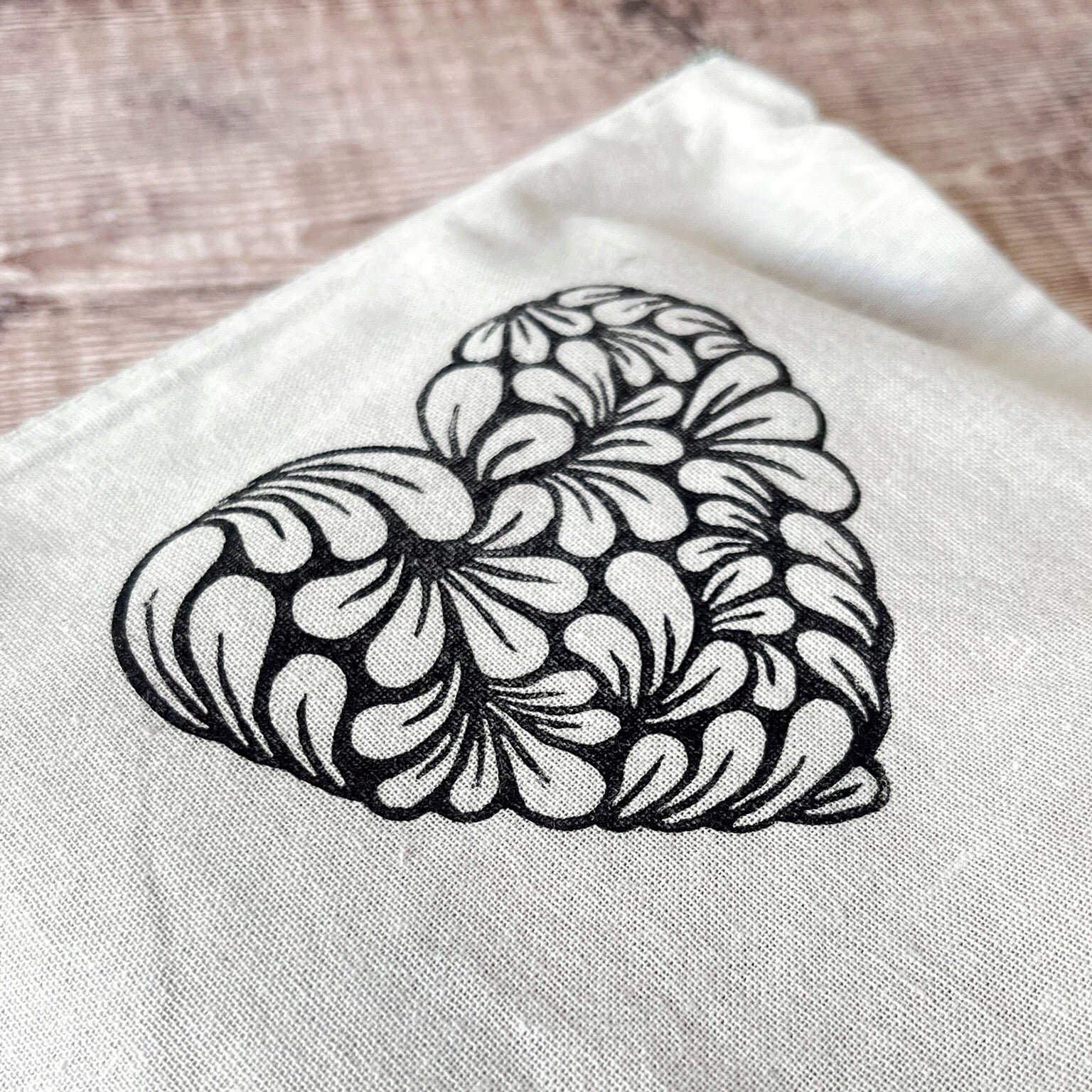 Close up of pale grey toiletry bag with lino printed heart design. Laid on a wooden surface.