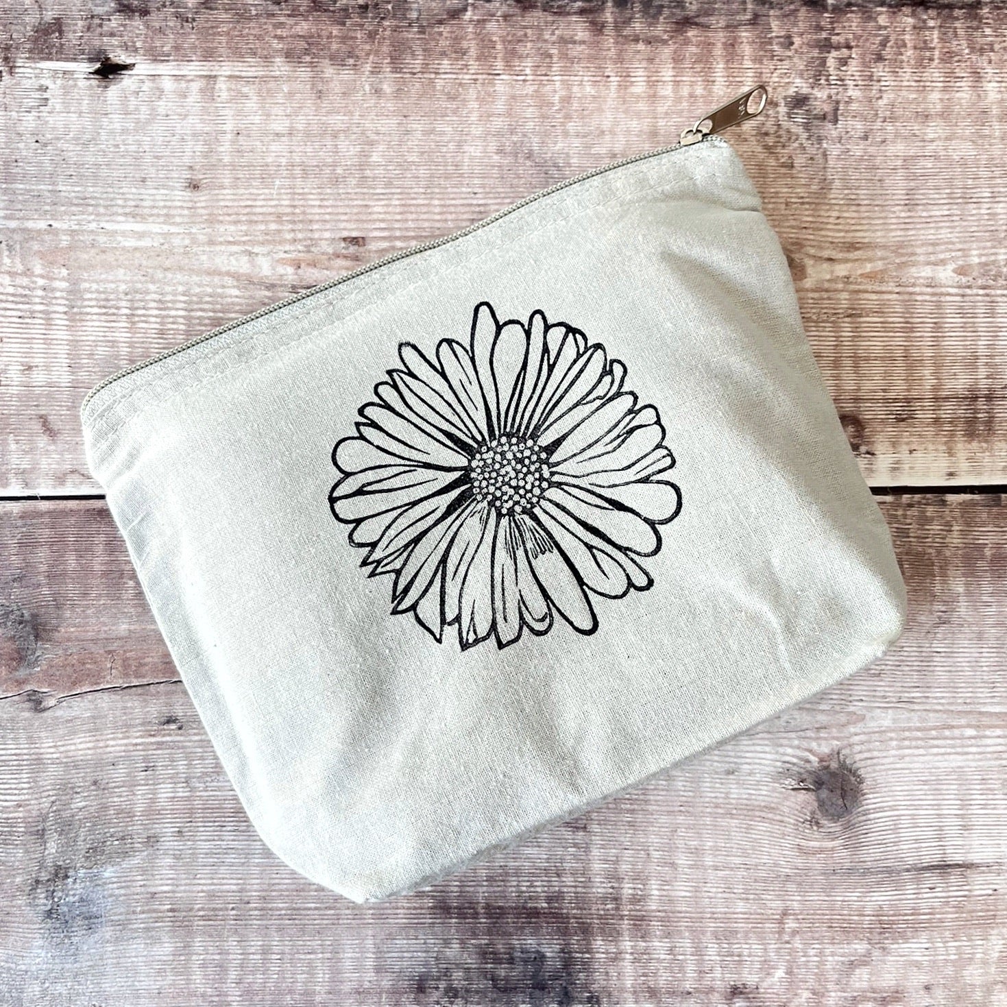 Pale grey cotton toiletry bag with a Daisy lino print laid on a wooden surface. 