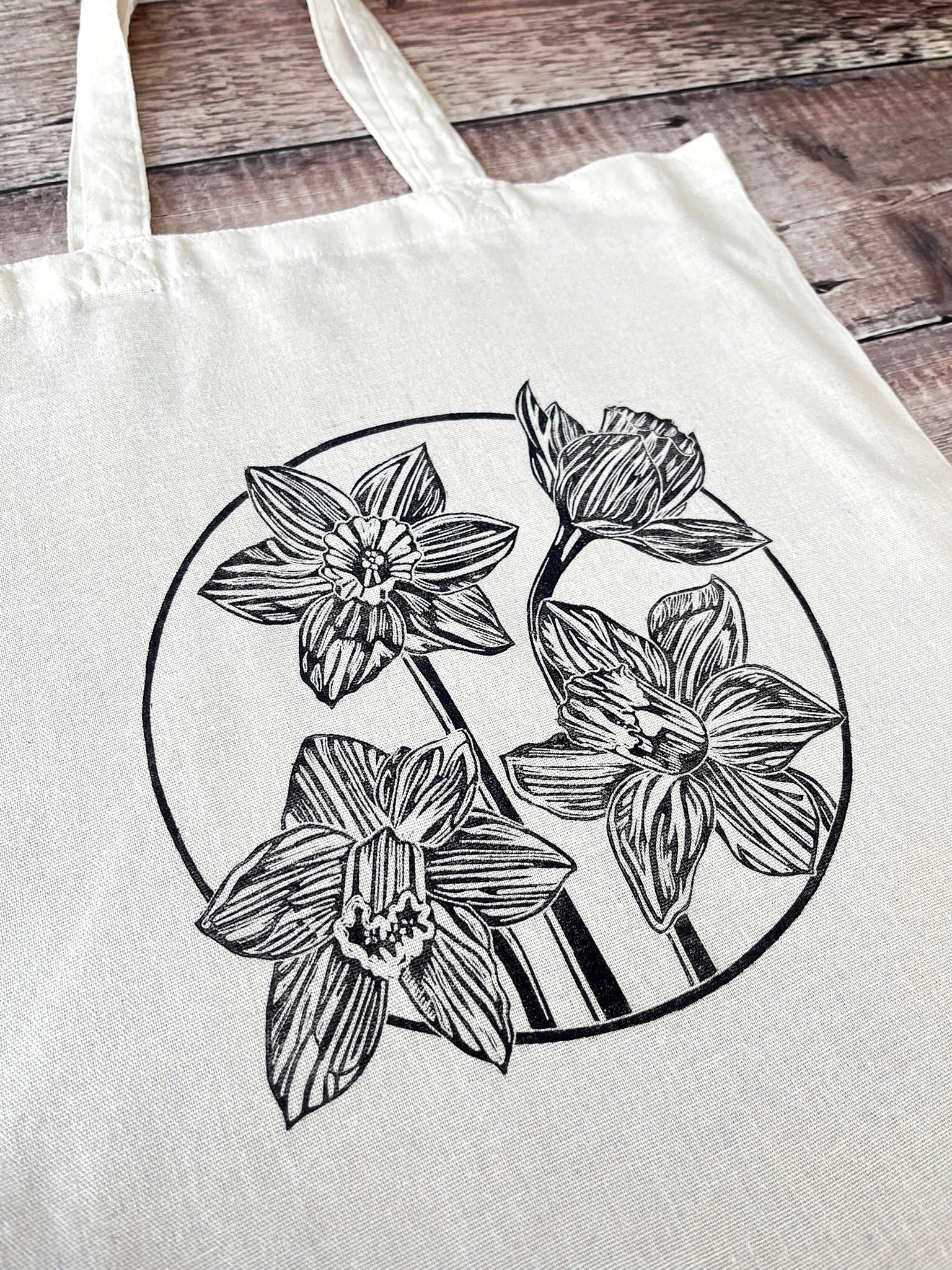 Close up of cream cotton tote bag with a lino printed Daffodils laid on a wooden surface