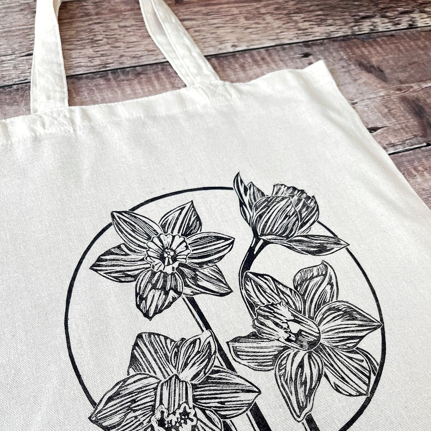 Close up of cream cotton tote bag with a lino printed Daffodils laid on a wooden surface