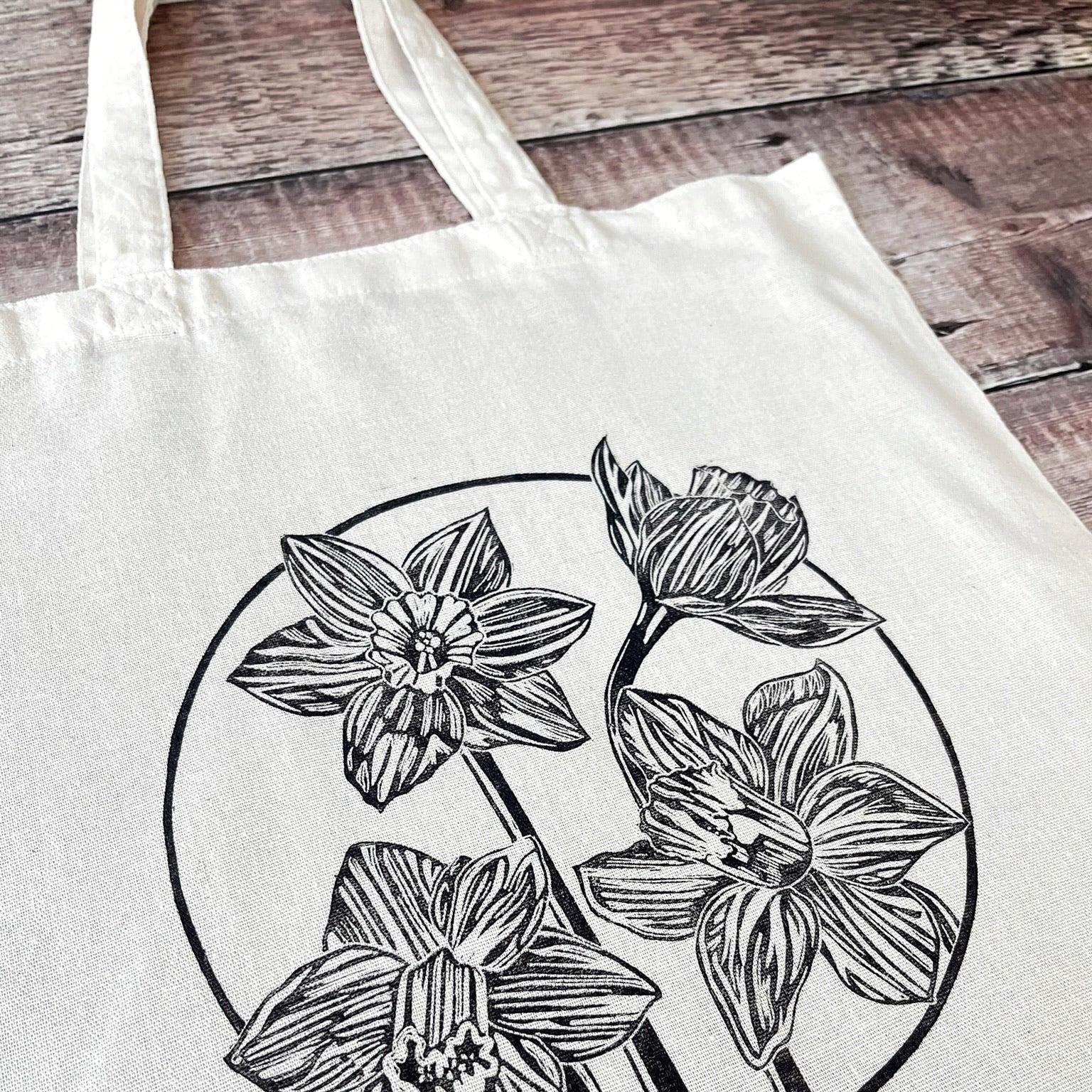 Close up of cream cotton tote bag with a lino printed Daffodils laid on a wooden surface
