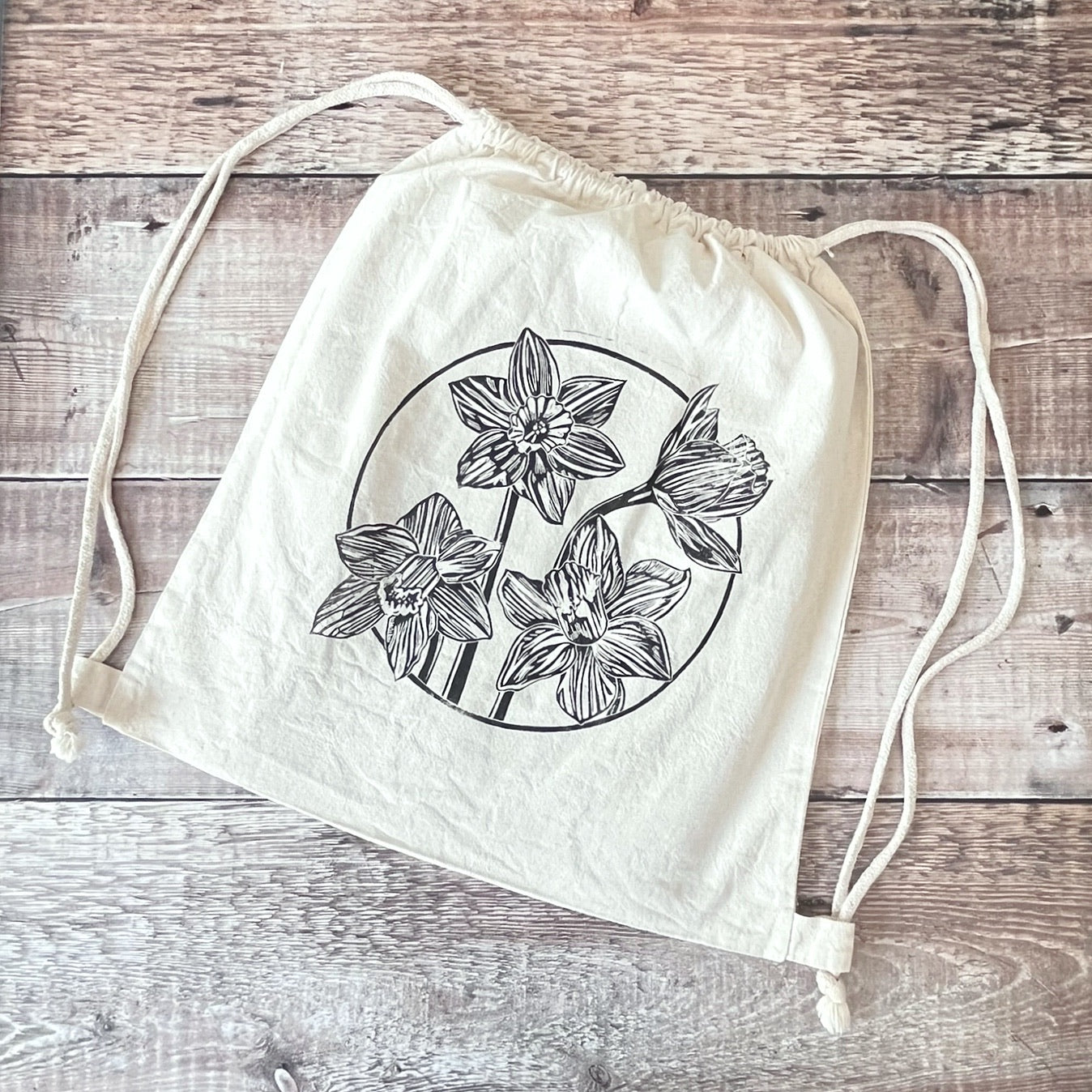 Lino print of Daffodils on a natural cotton drawstring bag laid on a wooden surface