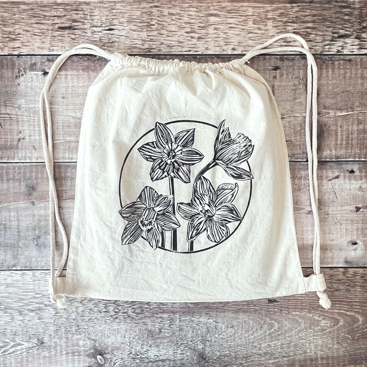 Lino print of Daffodils on a natural cotton drawstring bag laid on a wooden surface