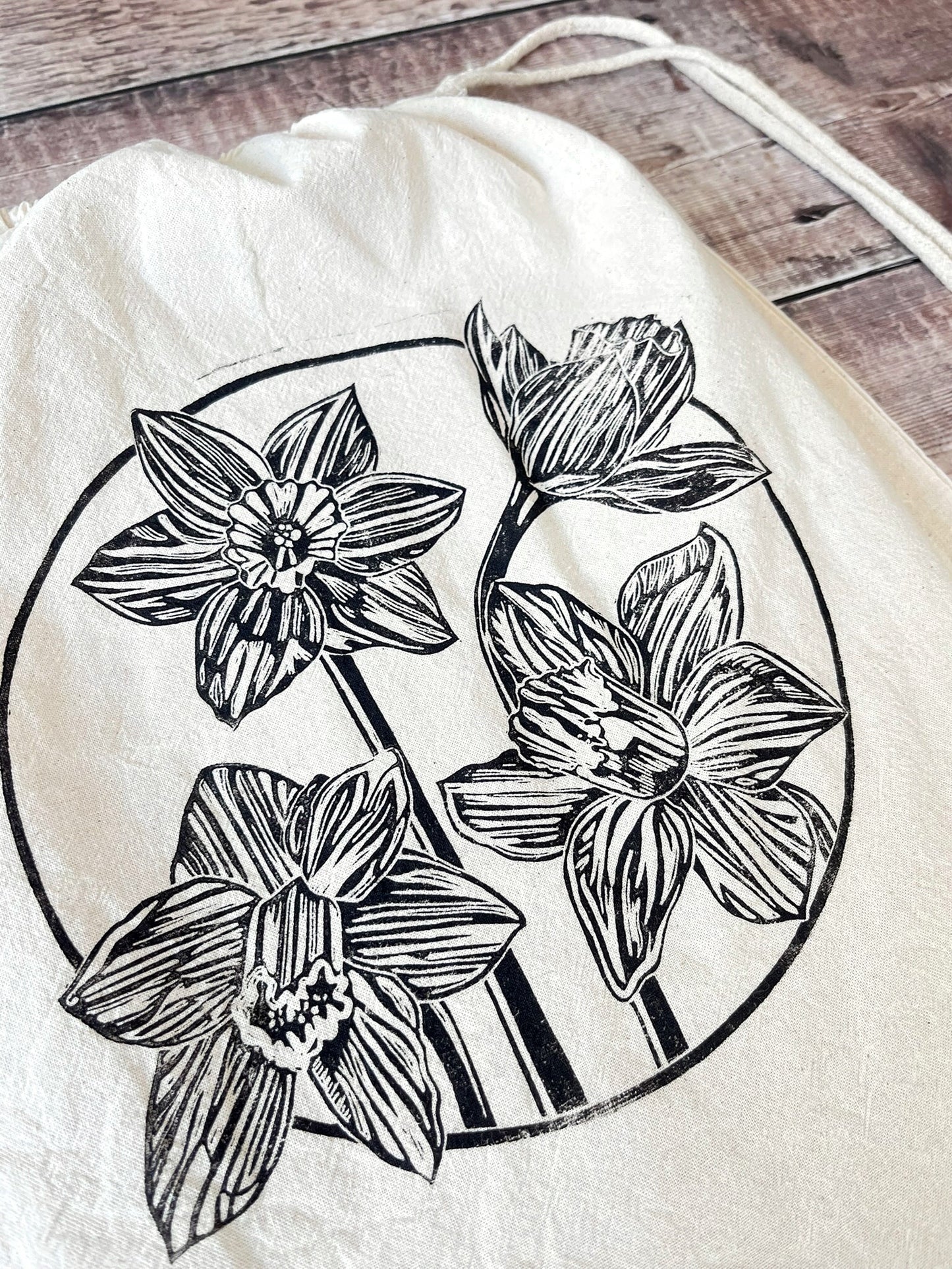 Close up of lino print of Daffodils on a natural cotton drawstring bag laid on a wooden surface