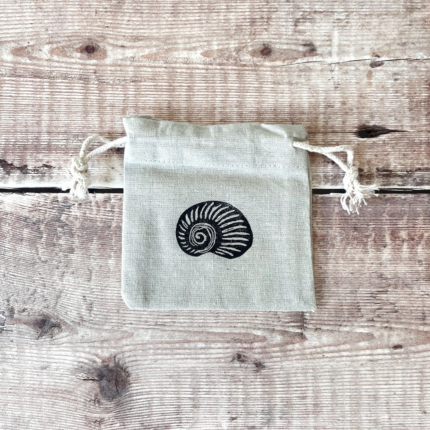 Grey drawstring cotton gift bags with a lino printed shell, laid flat on a wooden surface.