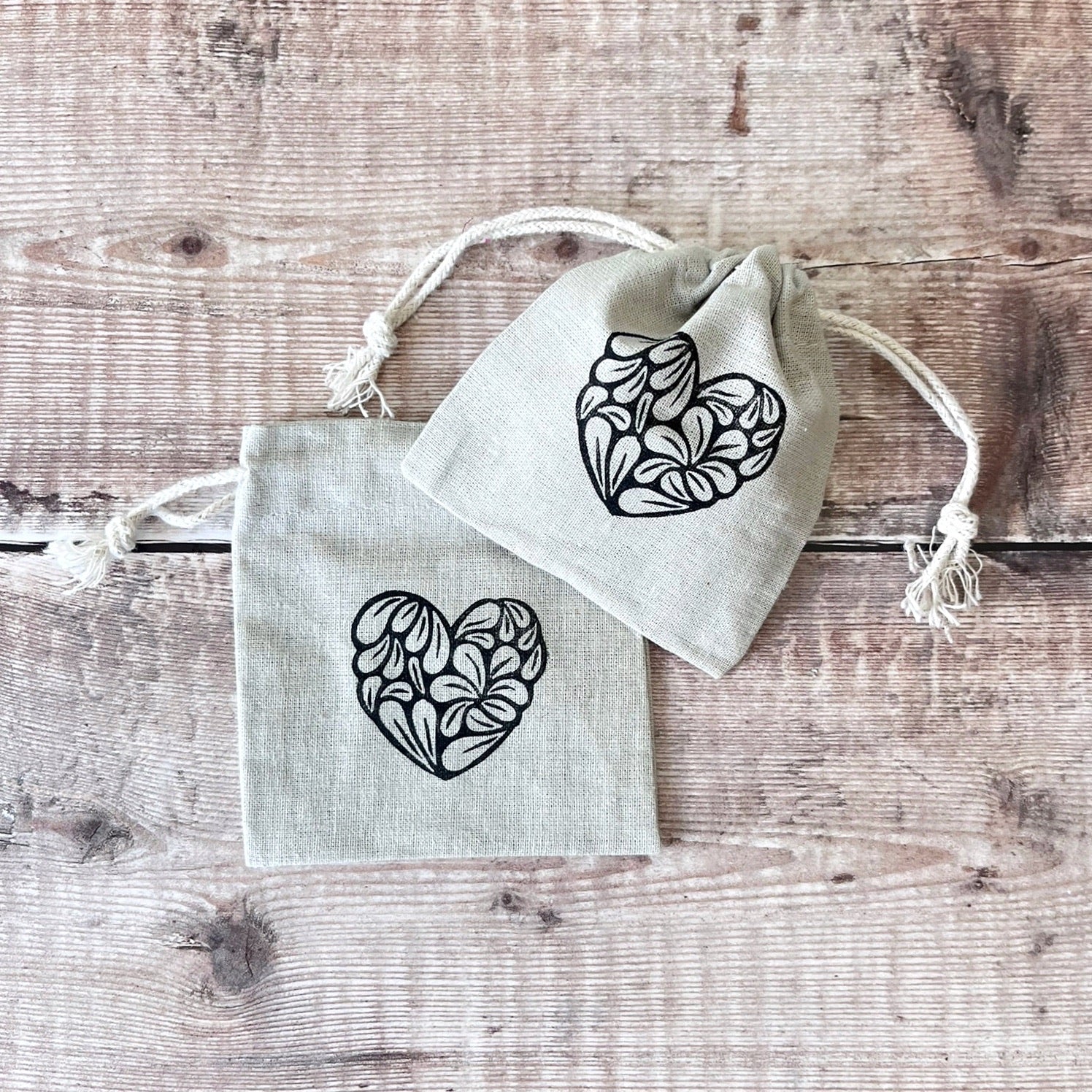 Two small drawstring bags with heart designs on a wooden surface