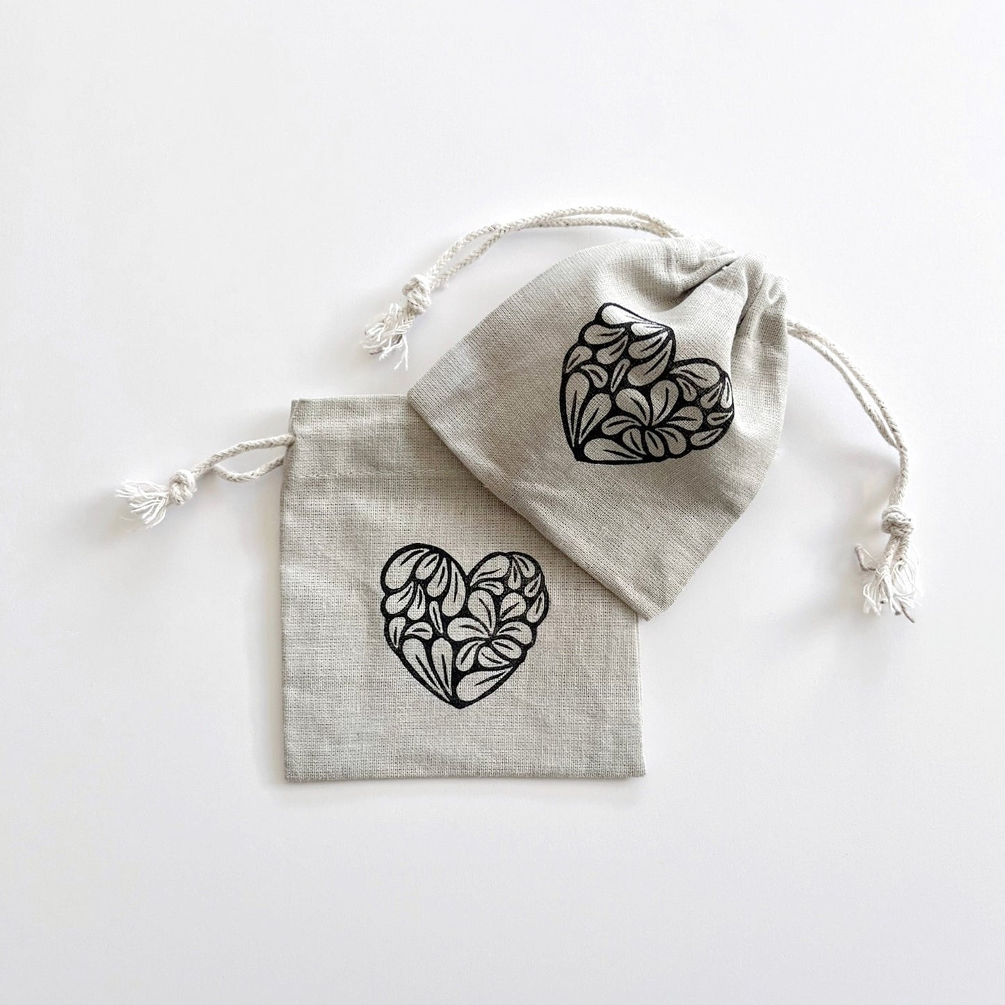 Two grey drawstring bags with black heart patterns laid on a white background